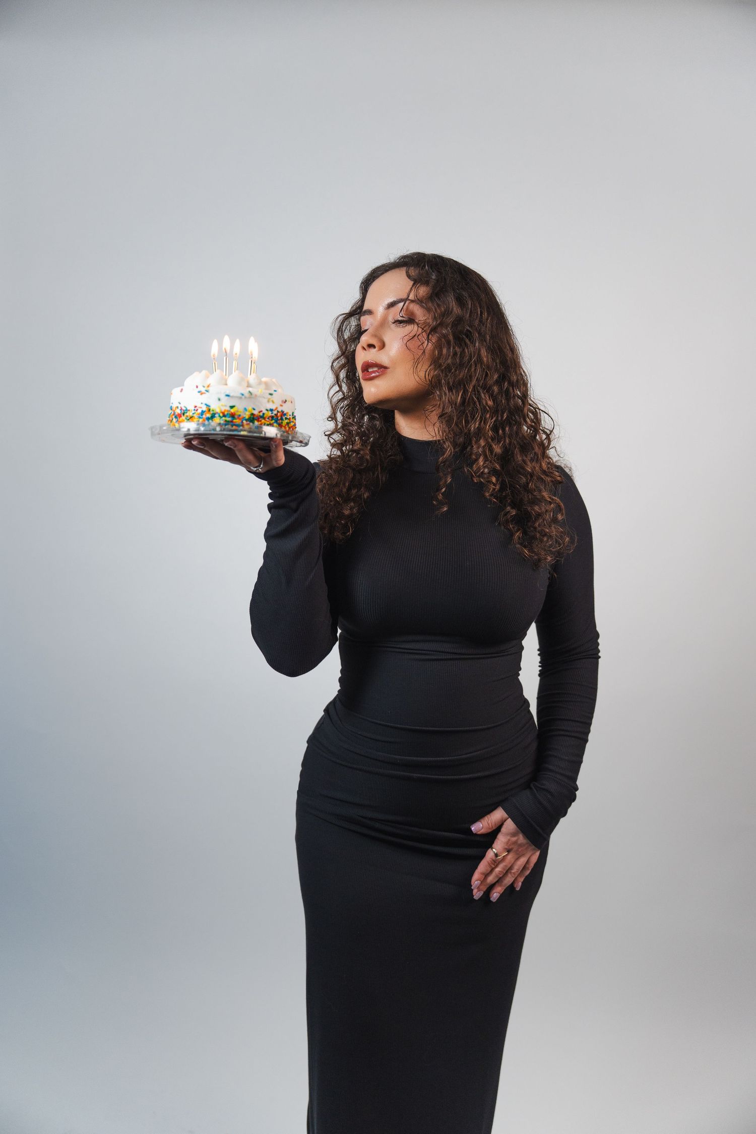 Woman in fitted black dress holding birthday cake during studio portrait session in South Florida