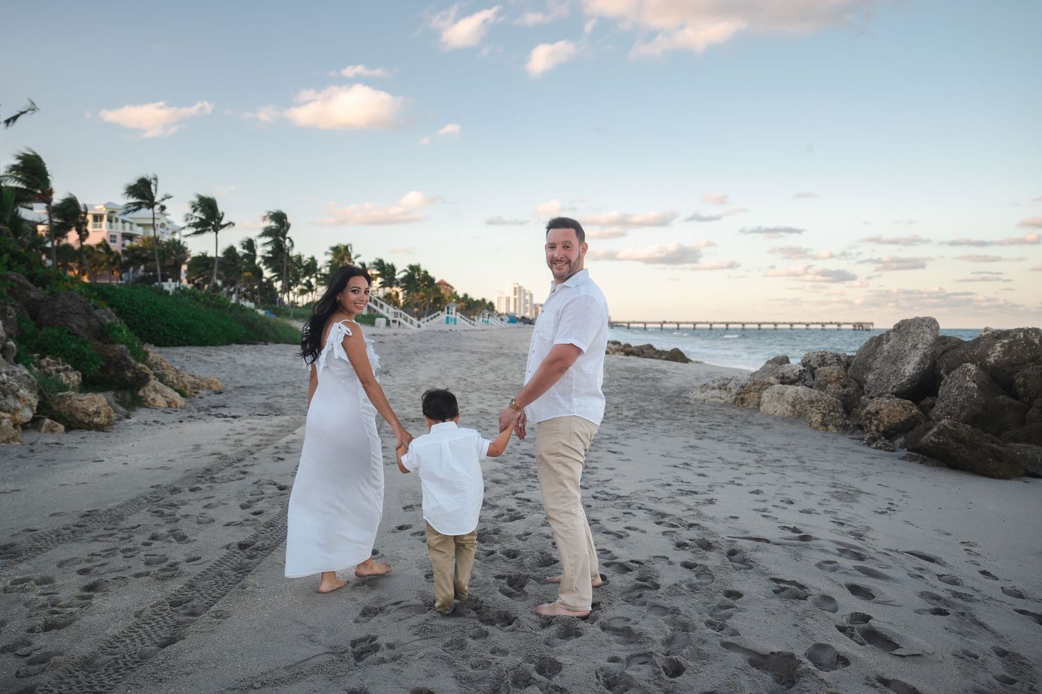 Family walking together on the beach during a pregnancy announcement session at sunset.