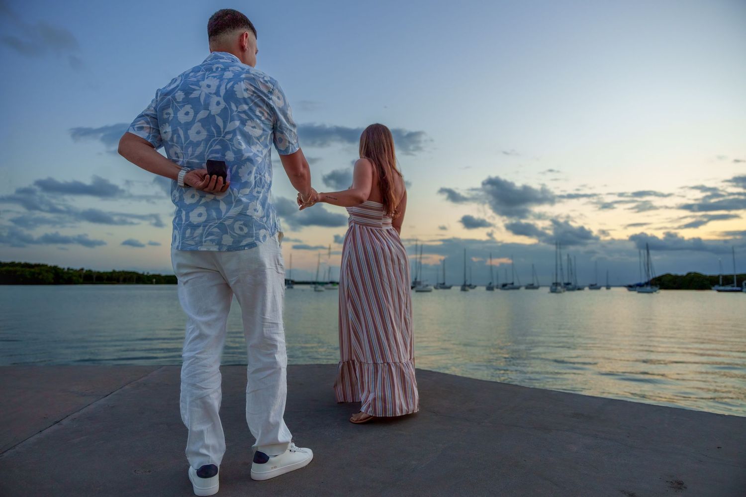 Wide shot of a couple standing together near the water after a proposal in Key Biscayne at sunset.