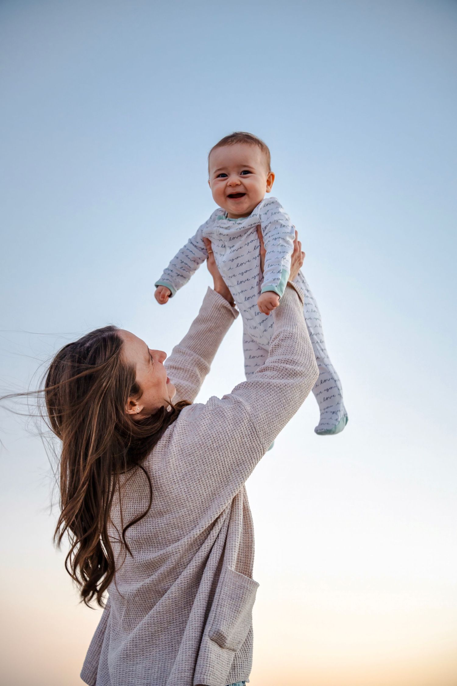 Candid moment of a mother lifting her baby into the air during a joyful beach family photo session in South Florida.