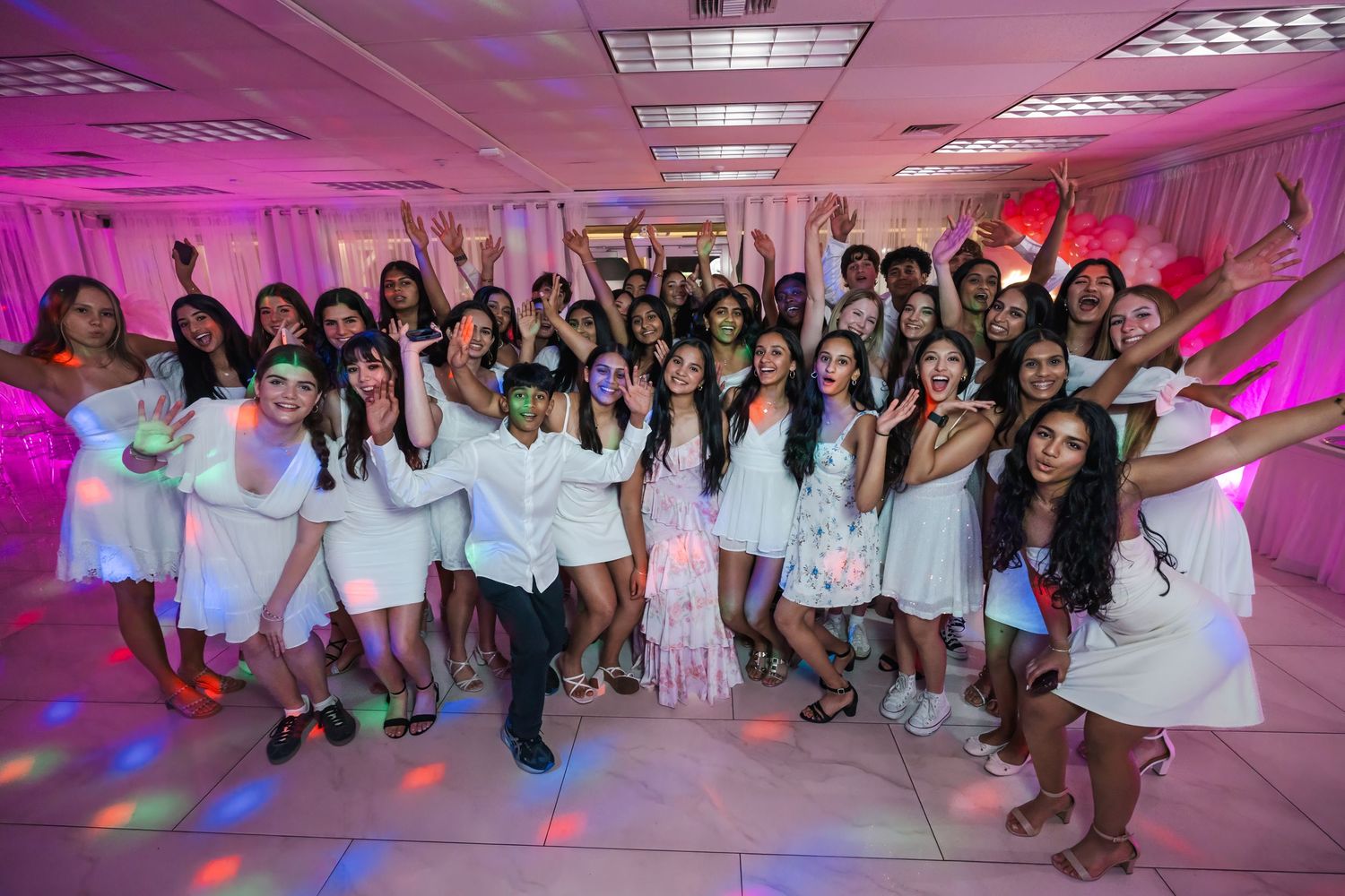 Large group of teens posing at a South Florida Sweet 16 celebration in white and pink outfits.