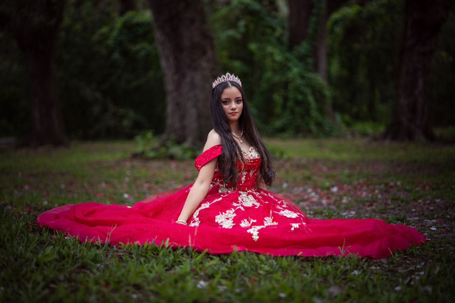 Outdoor Quinceañera session with flowing red gown, taken at a lush garden location.