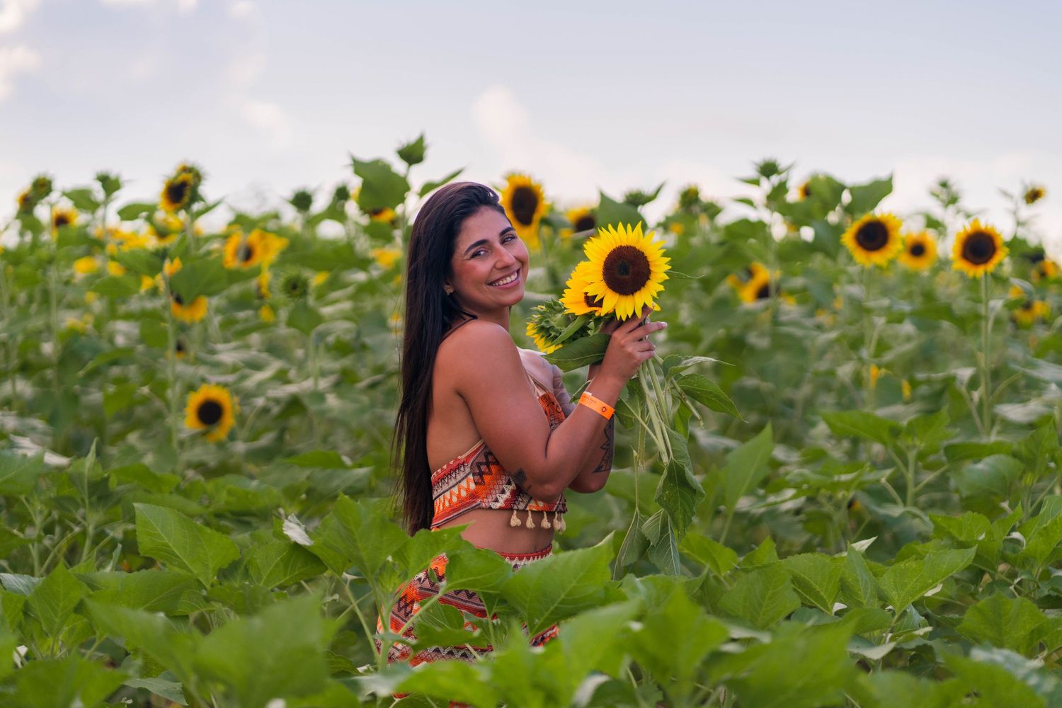 Sunflower field portrait session in South Florida – woman holds a bouquet of sunflowers, surrounded by lush greenery.