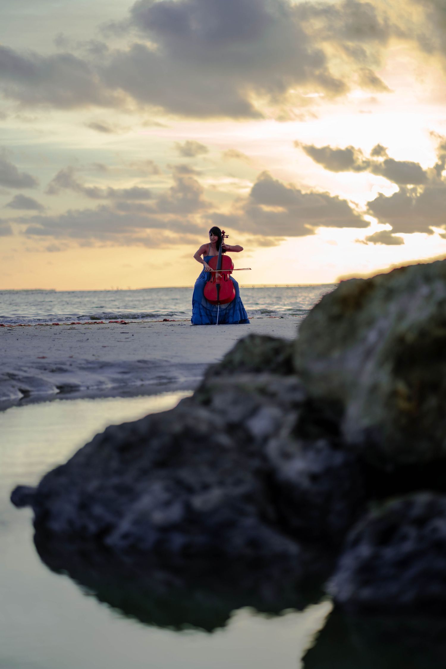 Cellist sitting on rocks at sunset during South Florida beach portrait session