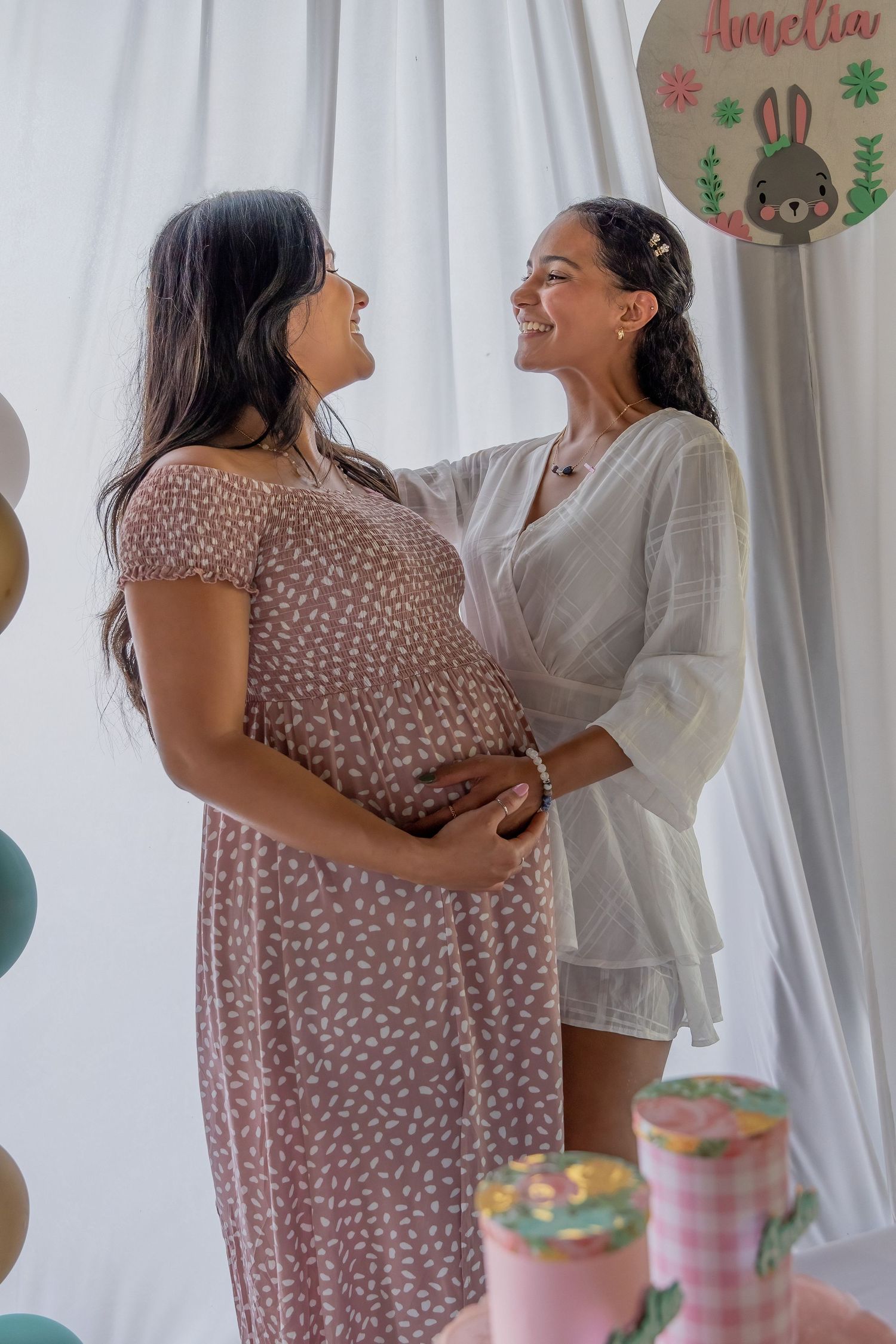 Two friends sharing a quiet moment during a maternity celebration, photographed indoors with soft natural light.