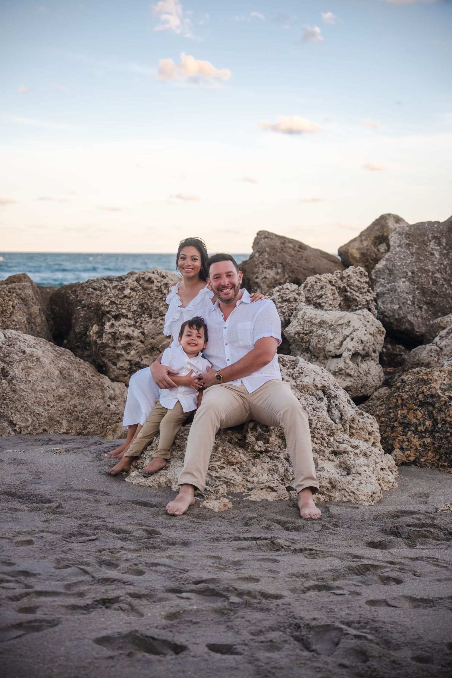 Family seated together on coastal rocks during a beach pregnancy announcement photo session.