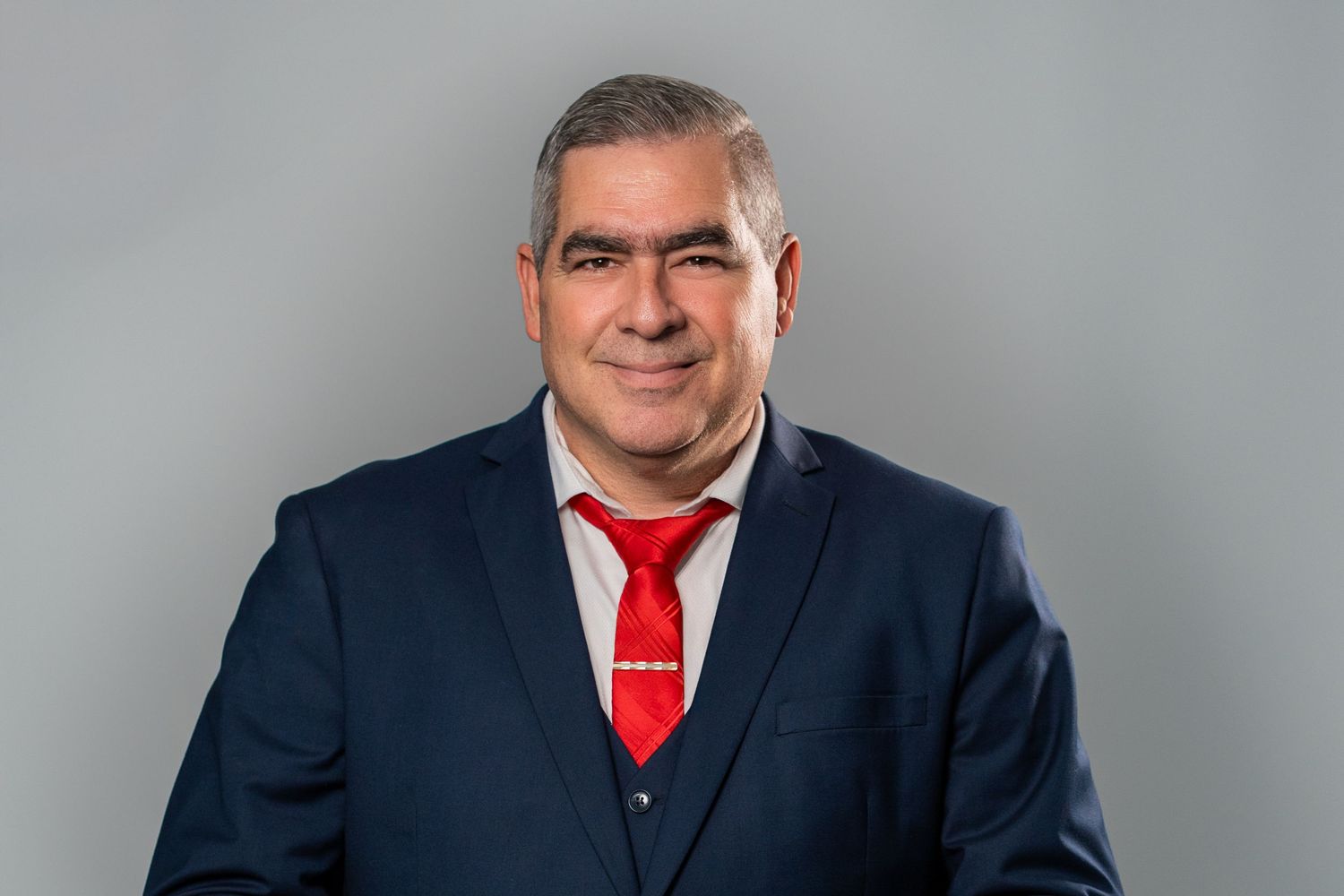 Smiling man in a navy blue suit and red tie during a studio headshot session.