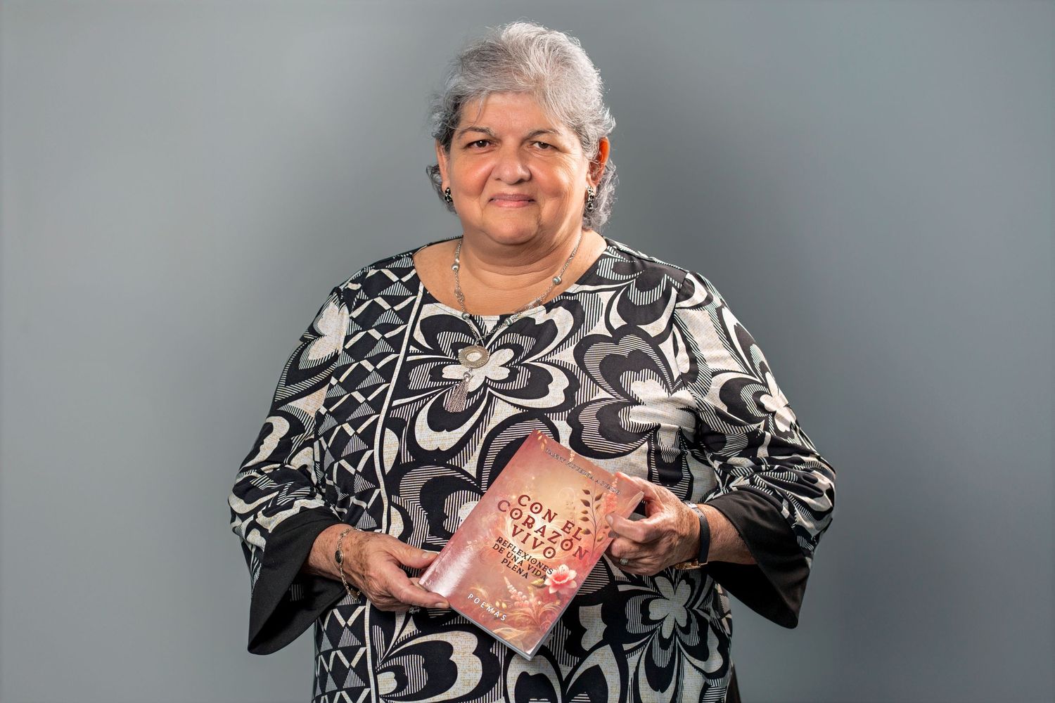 Older woman holding book during studio headshot session on gray background