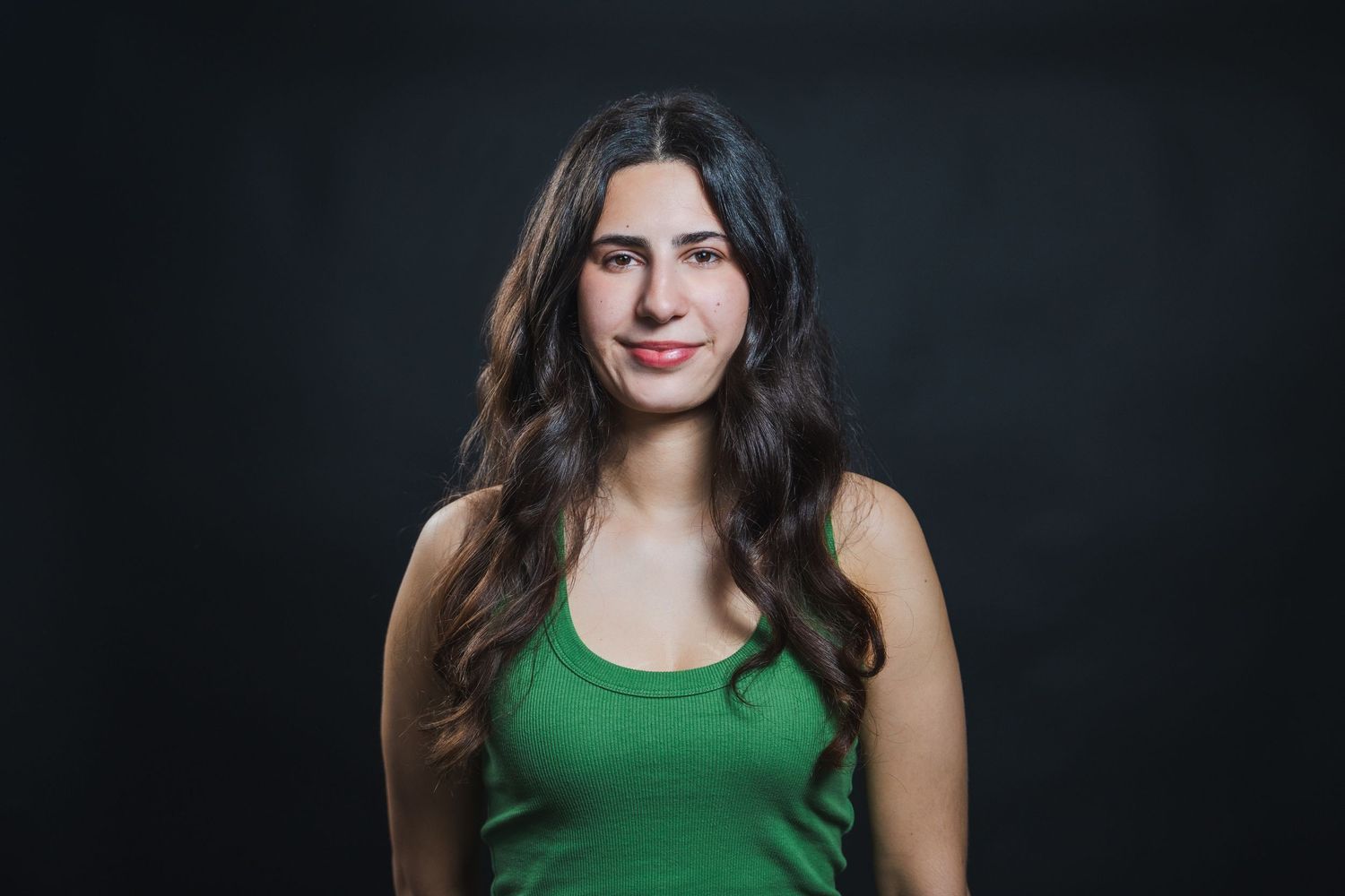 Professional acting headshot of a woman in a green top with soft studio lighting against a dark background.