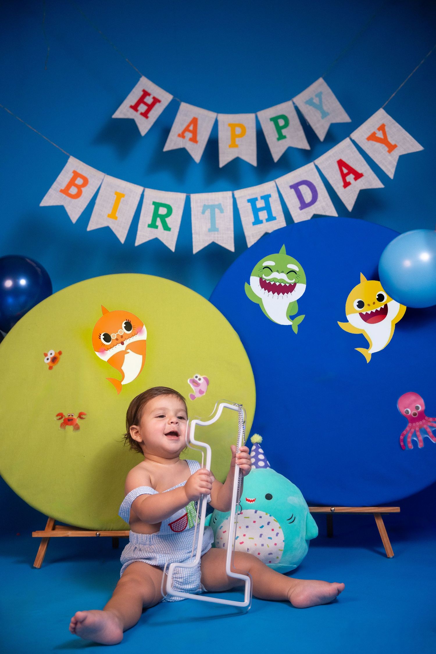 Toddler sitting beneath a birthday banner during a first birthday cake smash photo session.