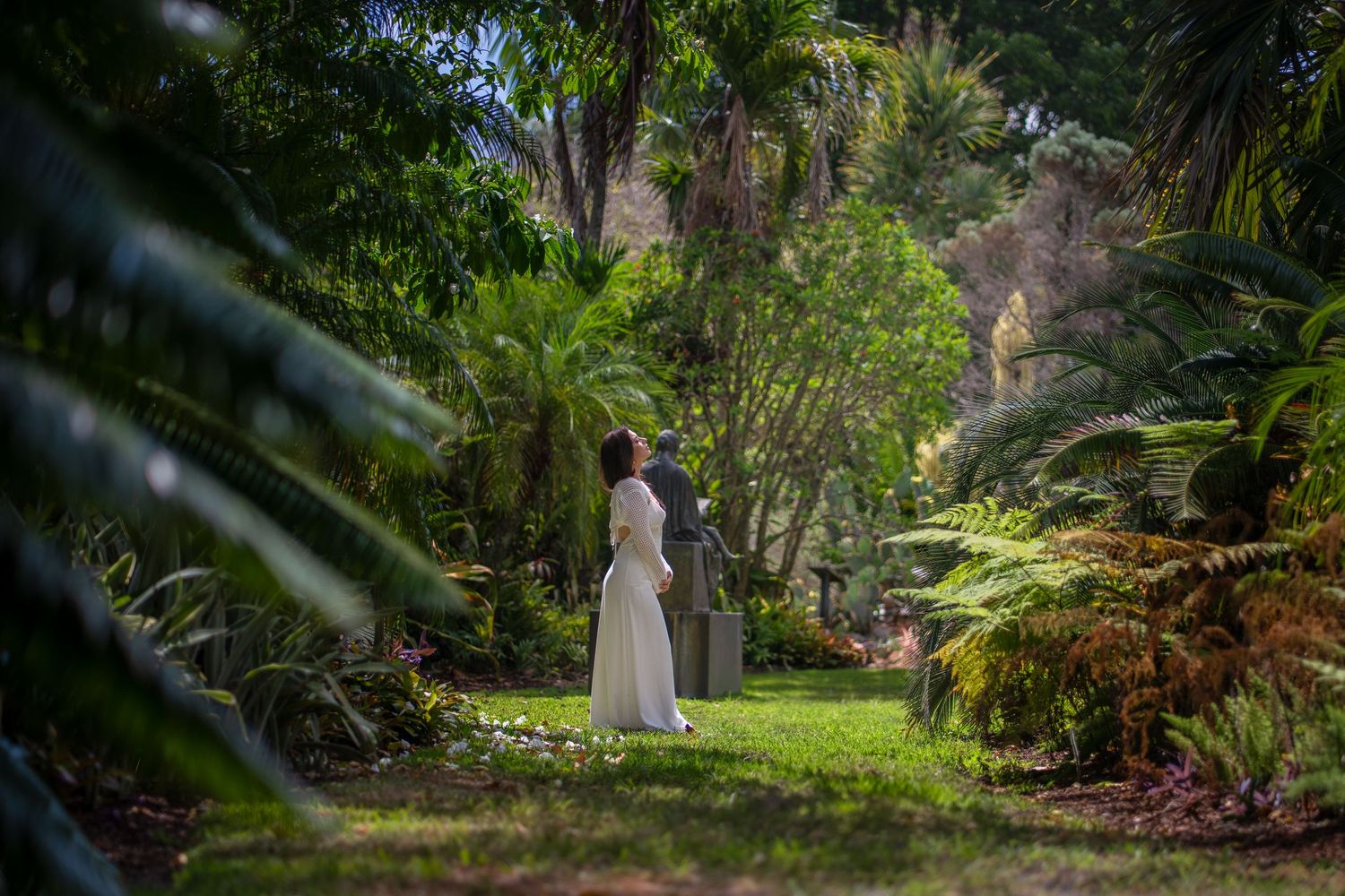 Full-body portrait of woman in white dress walking through tropical garden pathway