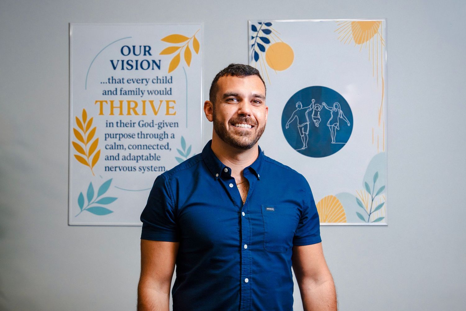Male chiropractor smiling in clinic space with branded vision poster displayed behind him during branding session