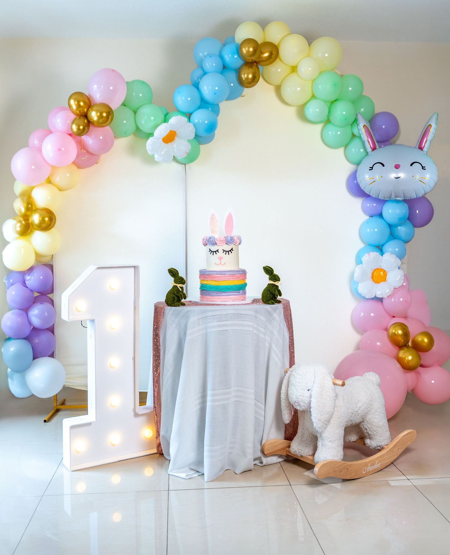 Pastel balloon arch and first birthday cake setup with bunny theme during a South Florida baby milestone photo session.