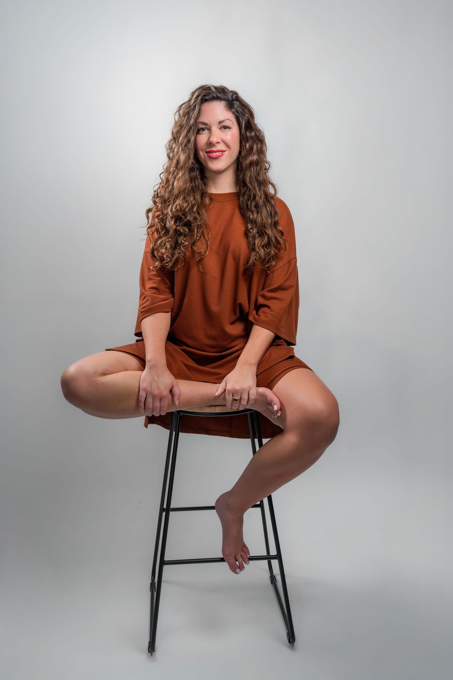 Professional headshot of woman seated on stool in clean white backdrop studio Miami Photographer