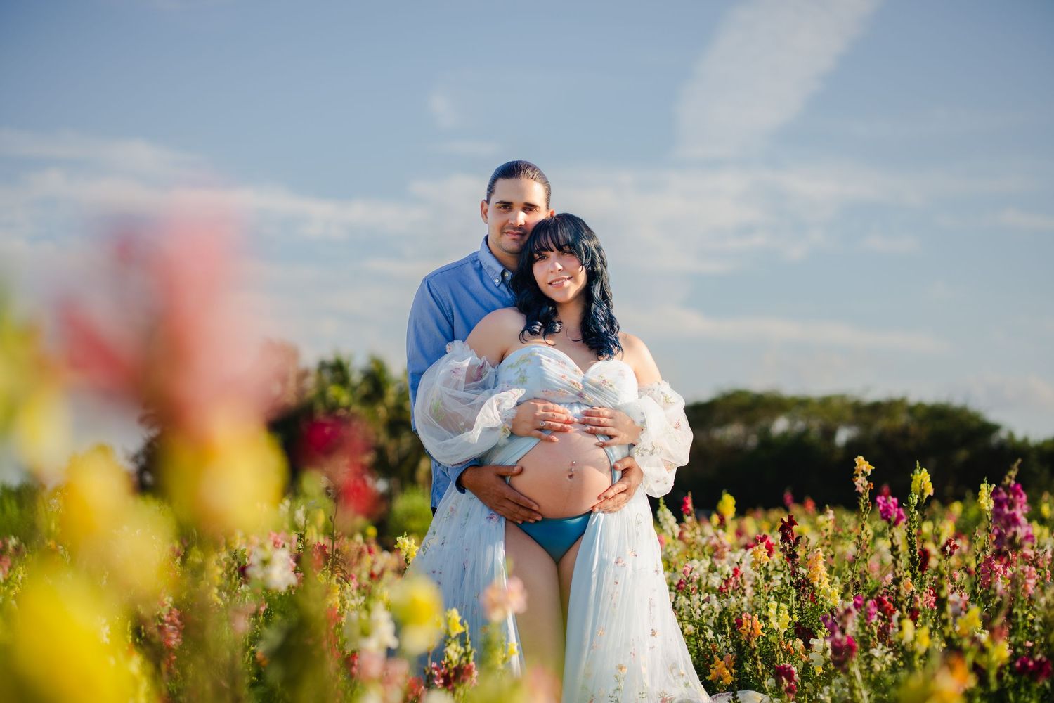 Outdoor maternity portrait of an expecting couple standing in a wildflower field during golden hour in South Florida.