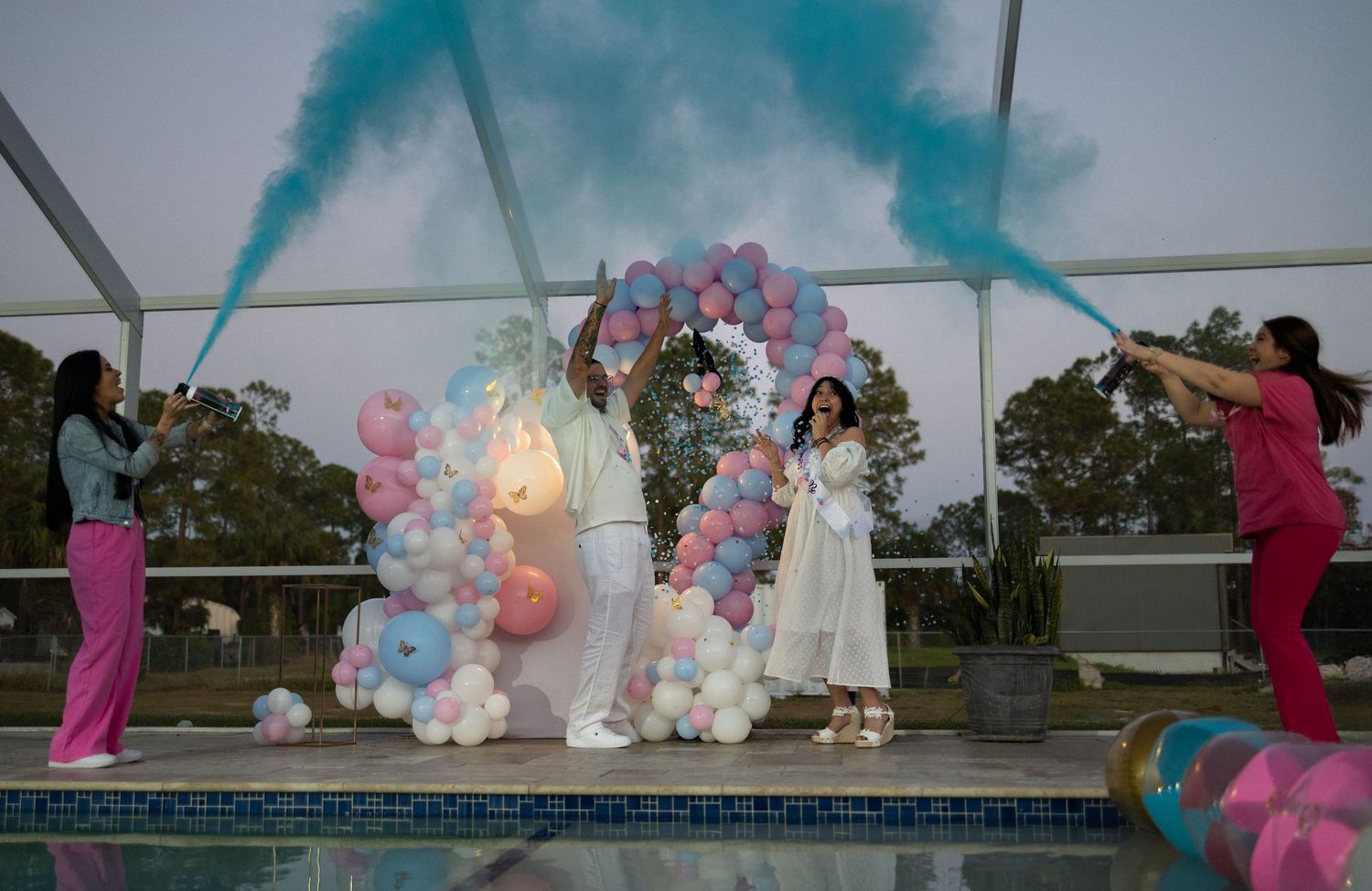 Gender reveal moment with blue smoke cannons and balloon arch at a poolside celebration in South Florida.