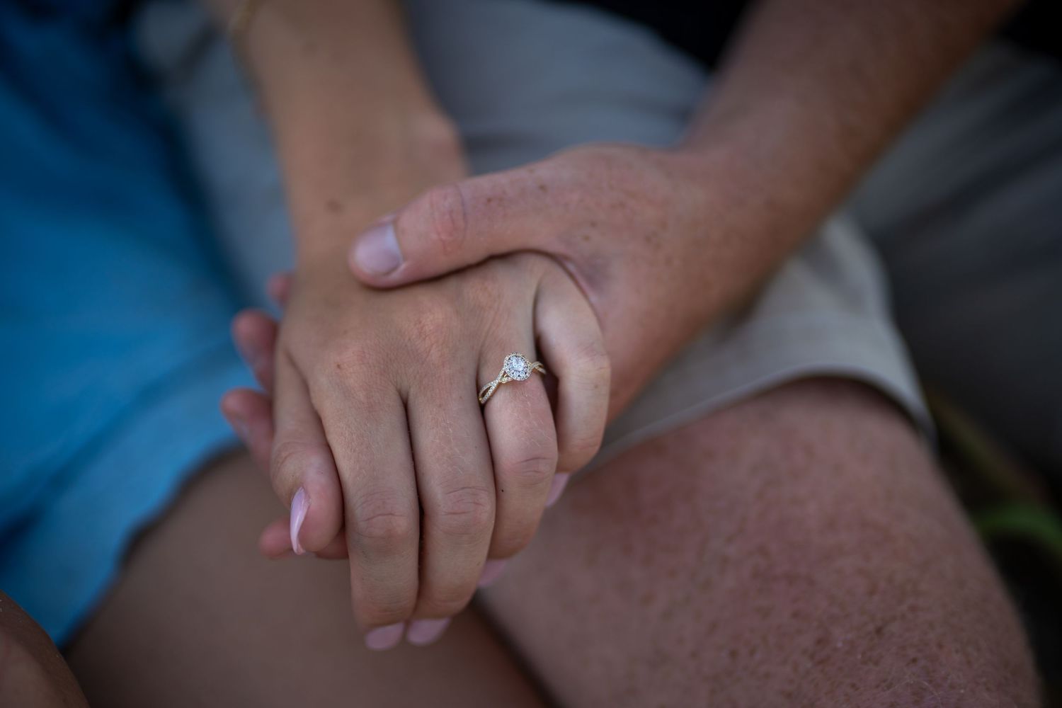 Detail photo of couple holding hands with engagement ring in focus