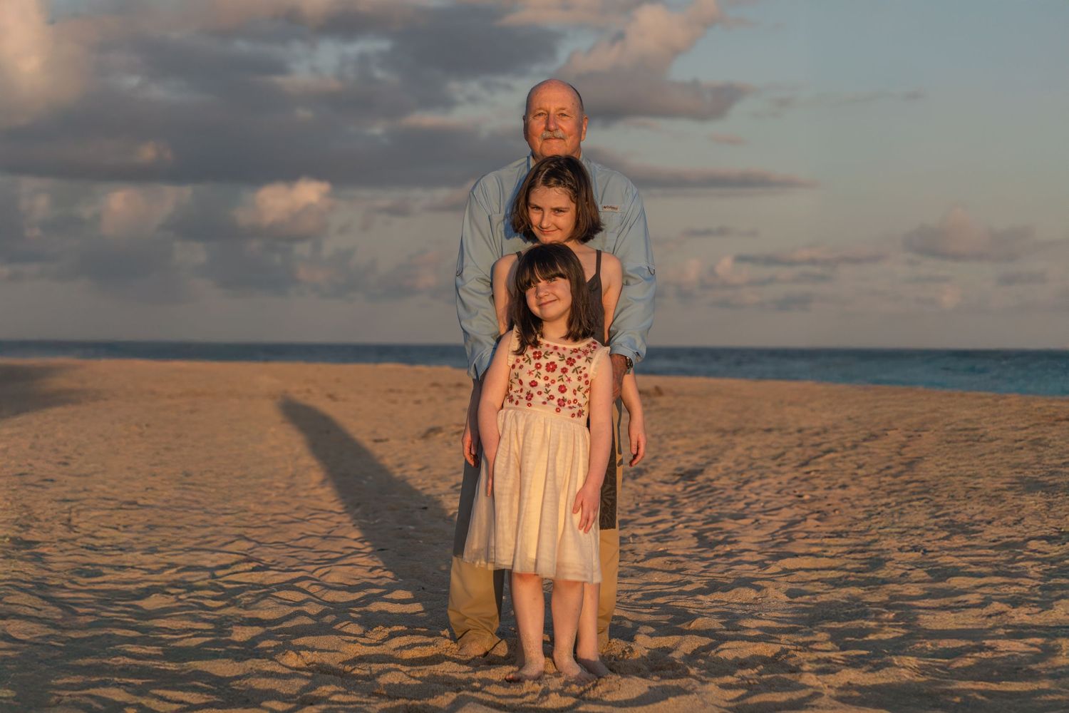 Grandfather with granddaugthers beach portrait in Palm Beach, FL – grandfather, mother, and daughter posing on the sand at golden hour.