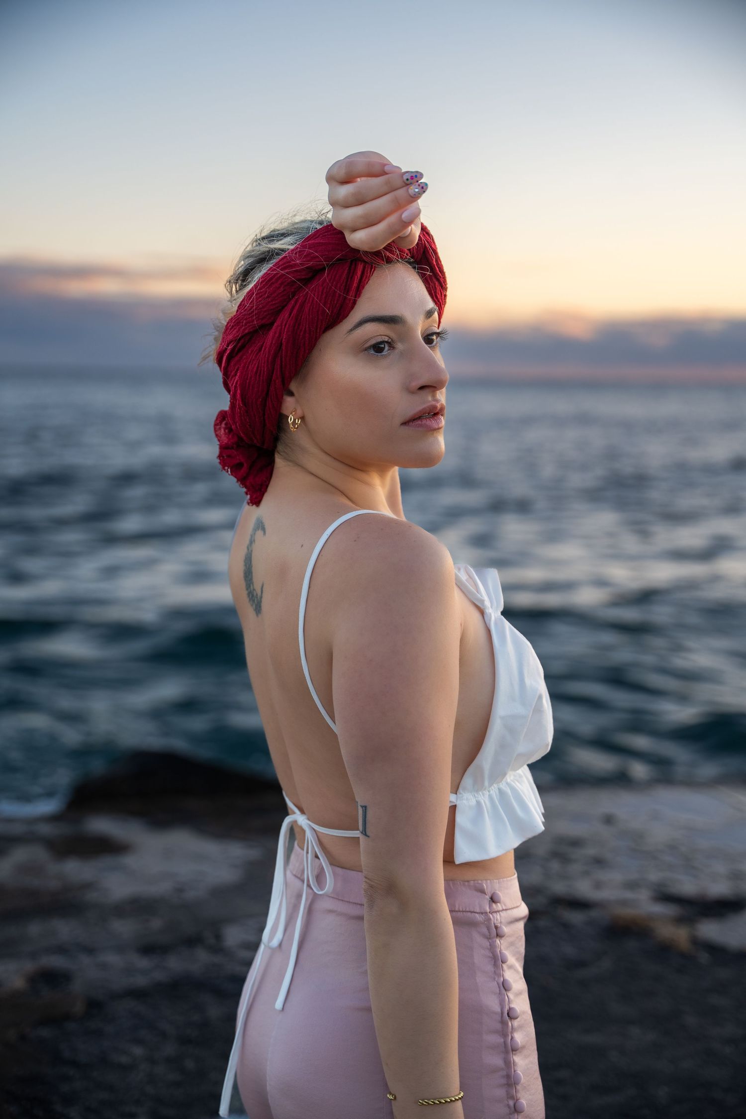 Moody oceanfront session in South Florida – a woman in a red headscarf and white blouse stands against a dramatic sky, wrapped in the fading