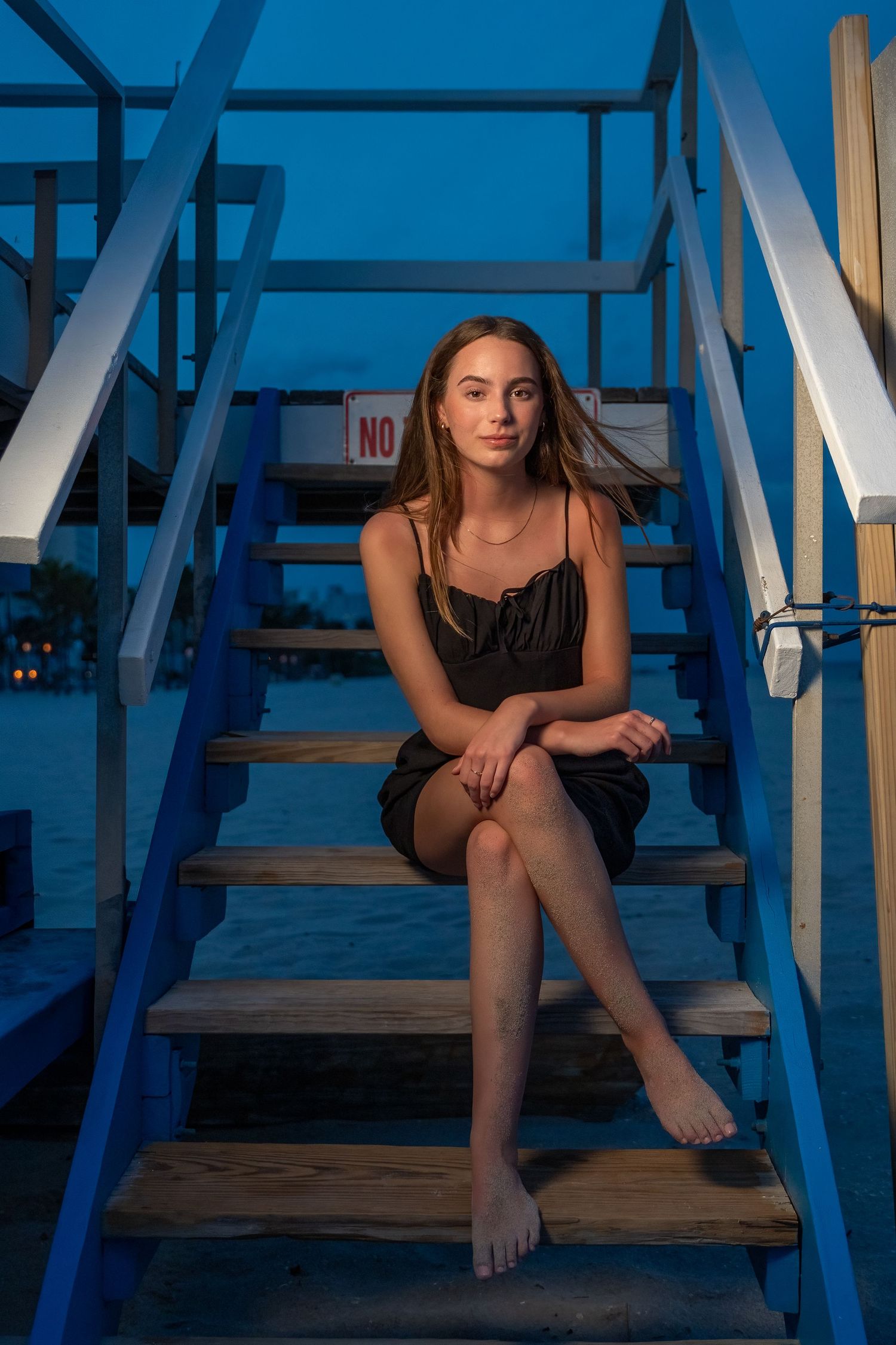 Senior girl poses on lifeguard stairs at the beach during sunset, capturing a cinematic moment for her graduation portraits in South Florida