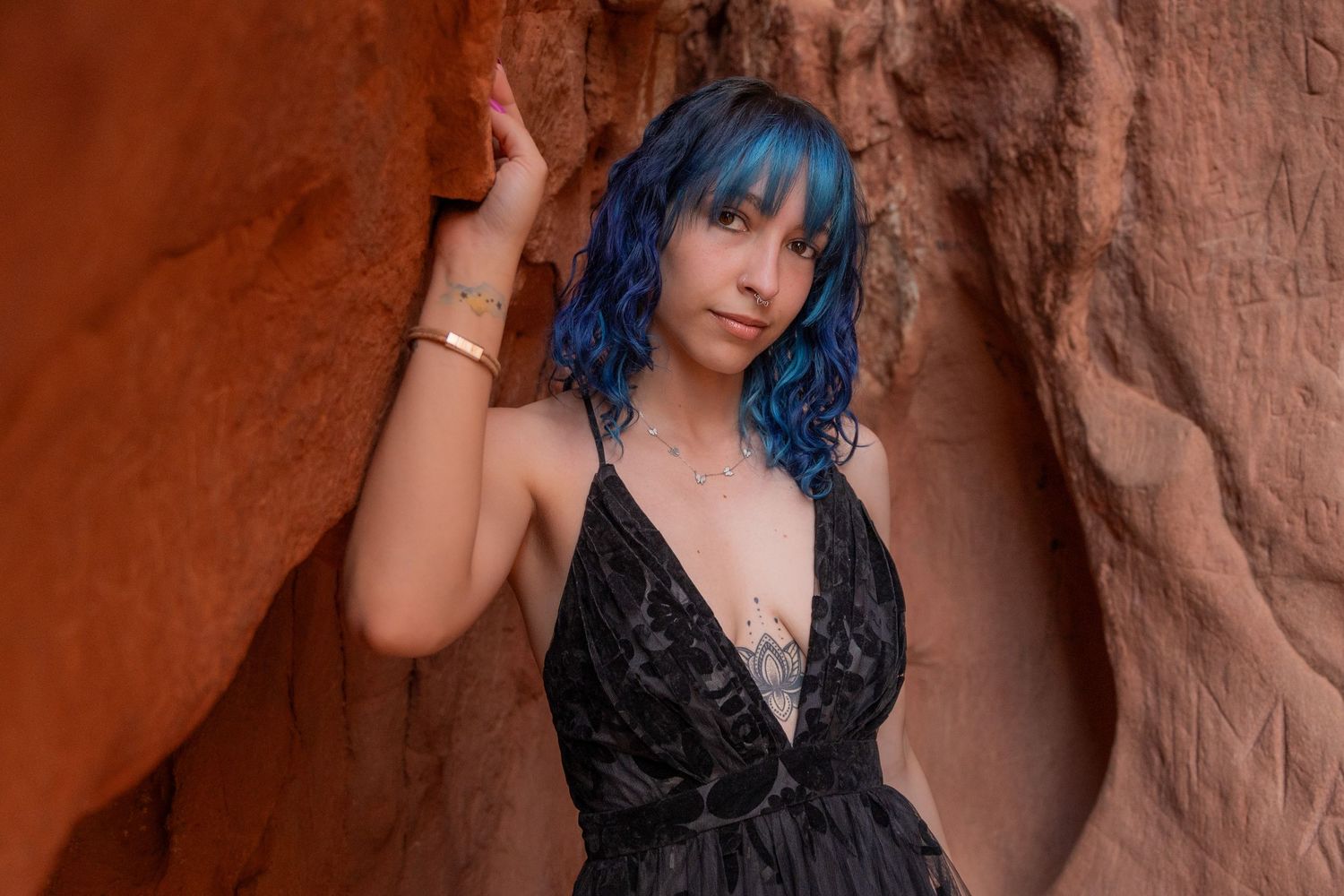 Ethereal portrait – blue-haired woman in a flowing gothic dress leans against the textured red rocks, exuding a moody and artistic vibe.