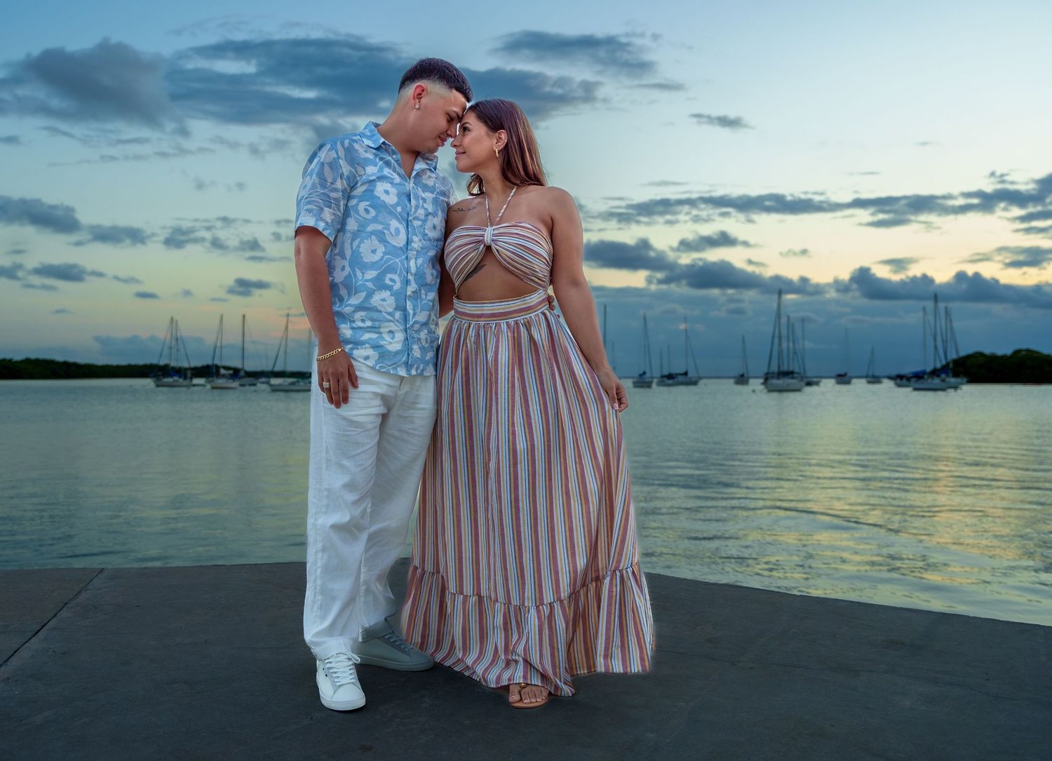 Newly engaged couple sharing a romantic moment by the water, celebrating love under a dreamy sunset sky.