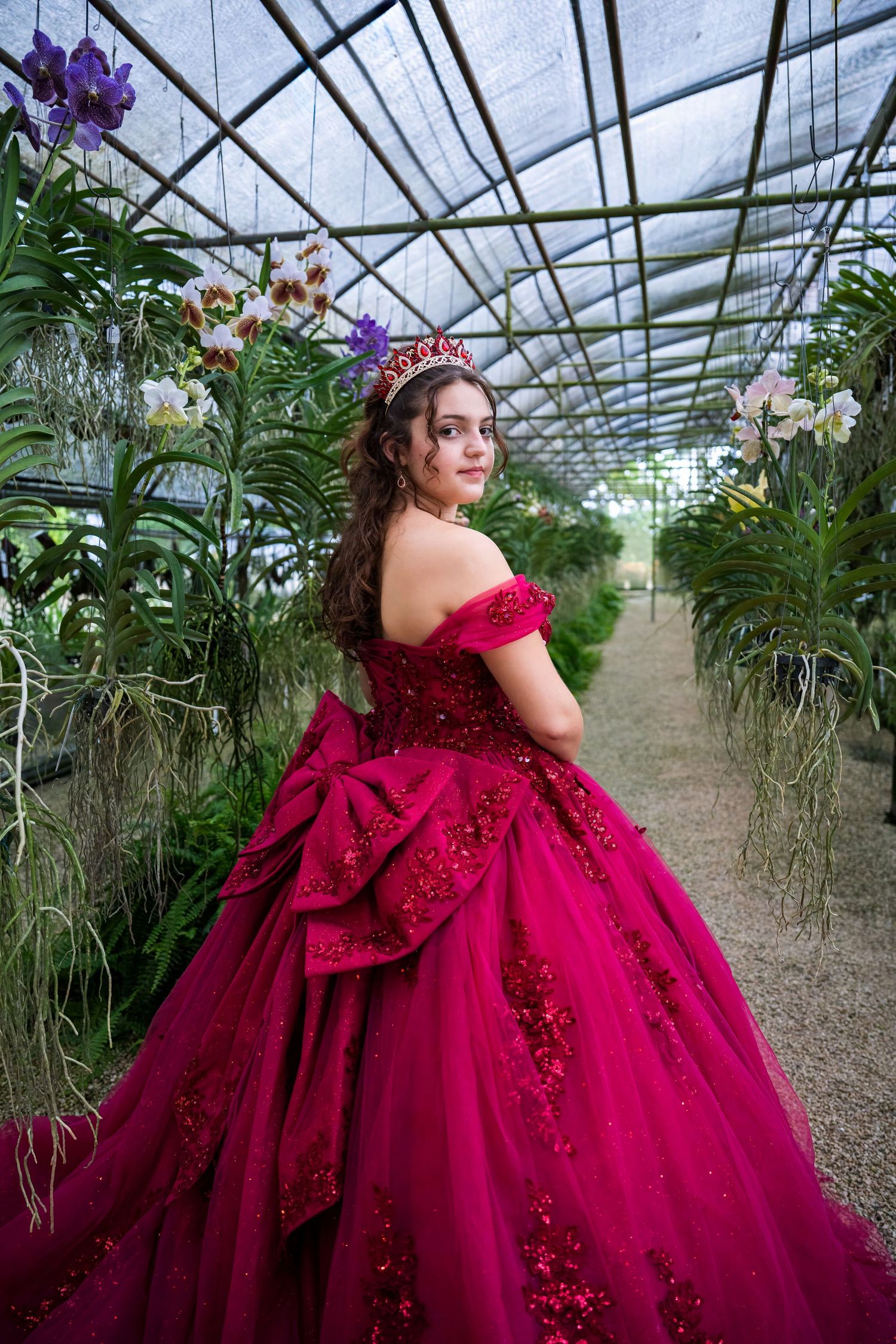 Quinceañera portrait featuring a burgundy ball gown and confident pose surrounded by tropical greenery.