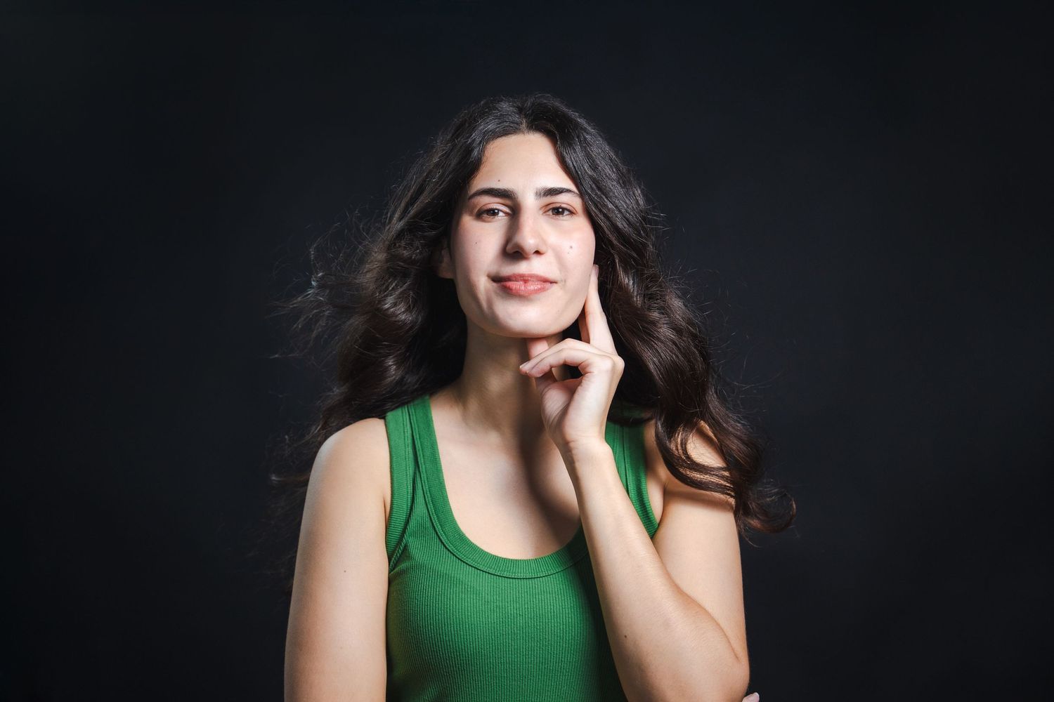 Editorial-style acting headshot of a woman resting her chin on her hand with soft studio lighting on a dark background.