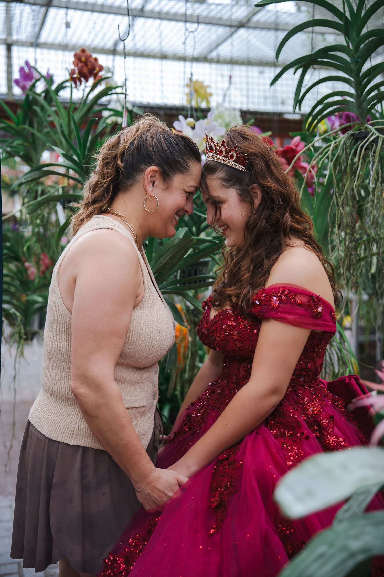 Quinceañera portrait of the celebrant and her date sharing a quiet moment inside a lush orchid greenhouse.