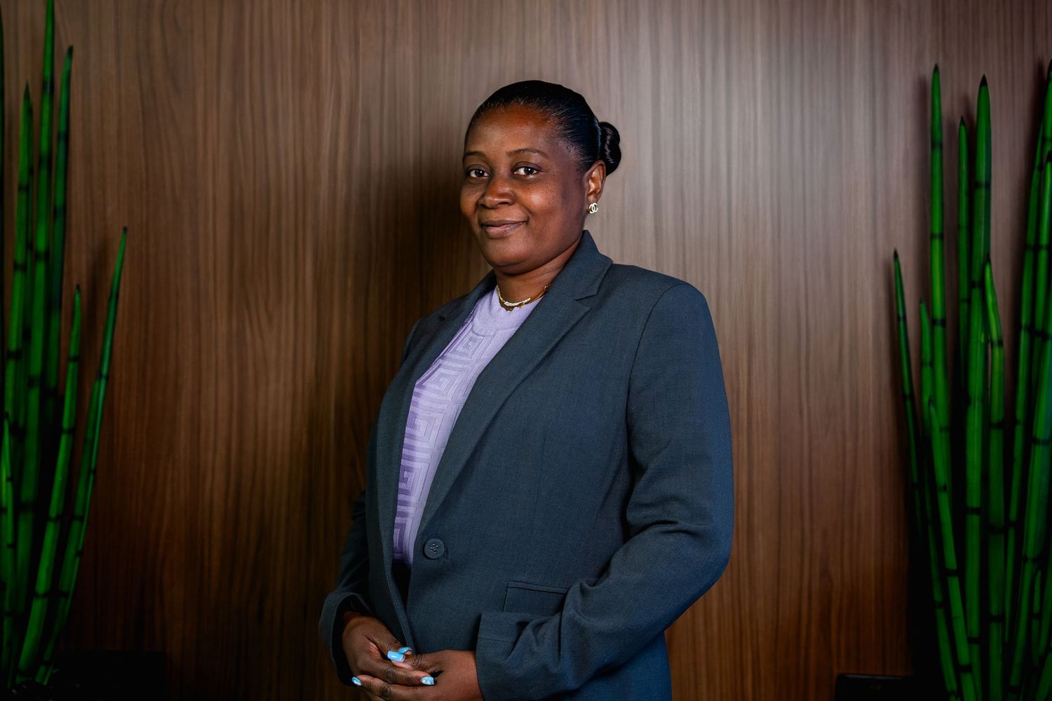 Professional woman in blazer standing against wood wall with plants