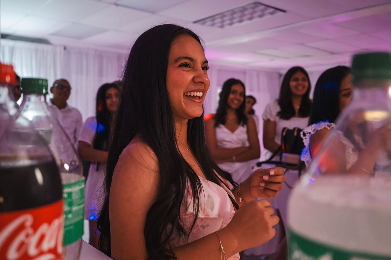Birthday girl smiling while standing near her cake and drinks during a celebration.
