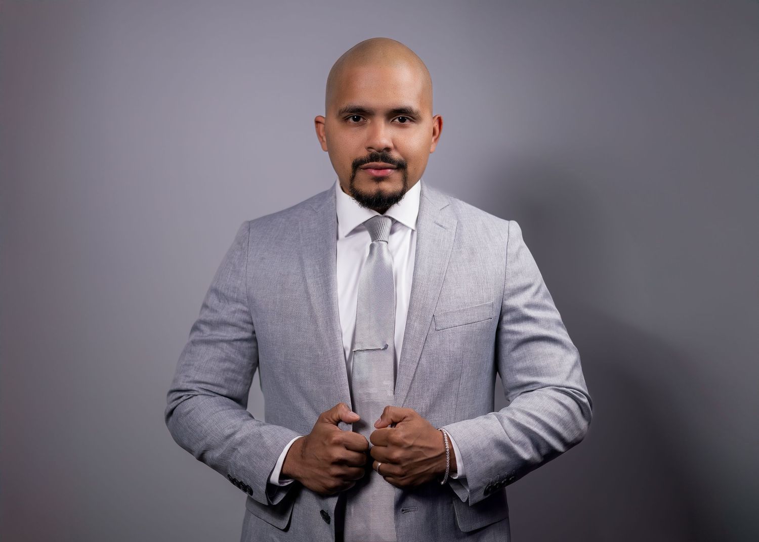 Confident man in a light gray suit adjusting his tie during a business branding shoot.