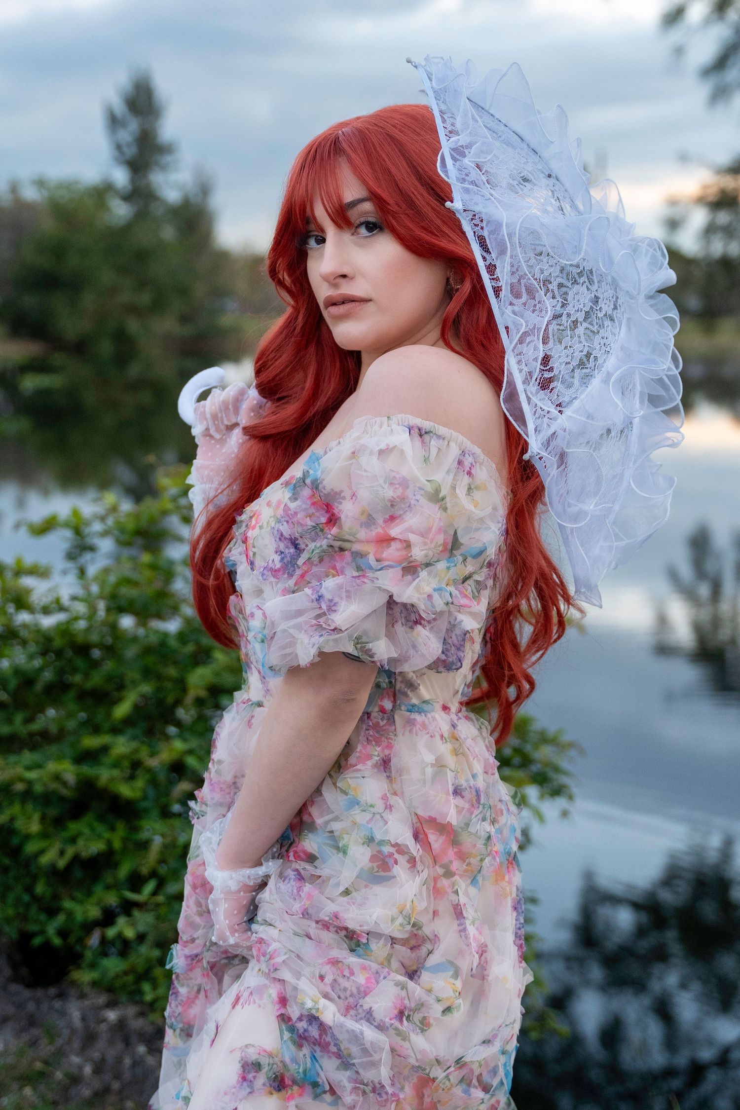 Elegant red-haired woman in a vintage floral gown and lace bonnet, evoking Victorian charm by a tranquil lakeside. Amelia Earhart Park