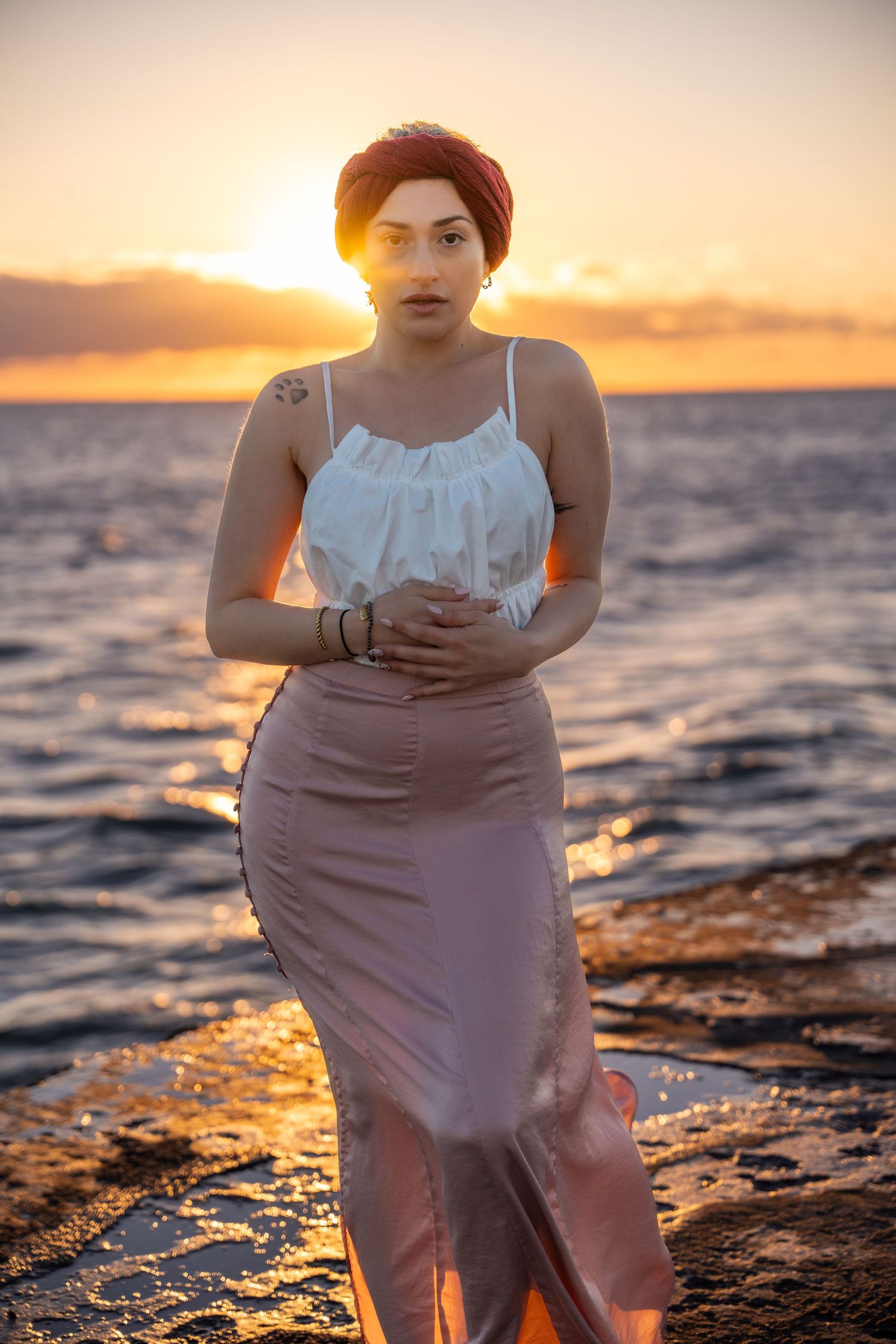 Sunset lifestyle session on Miami Beach – a woman in a white top and blush skirt stands on rocky shores, wrapped in soft evening light.