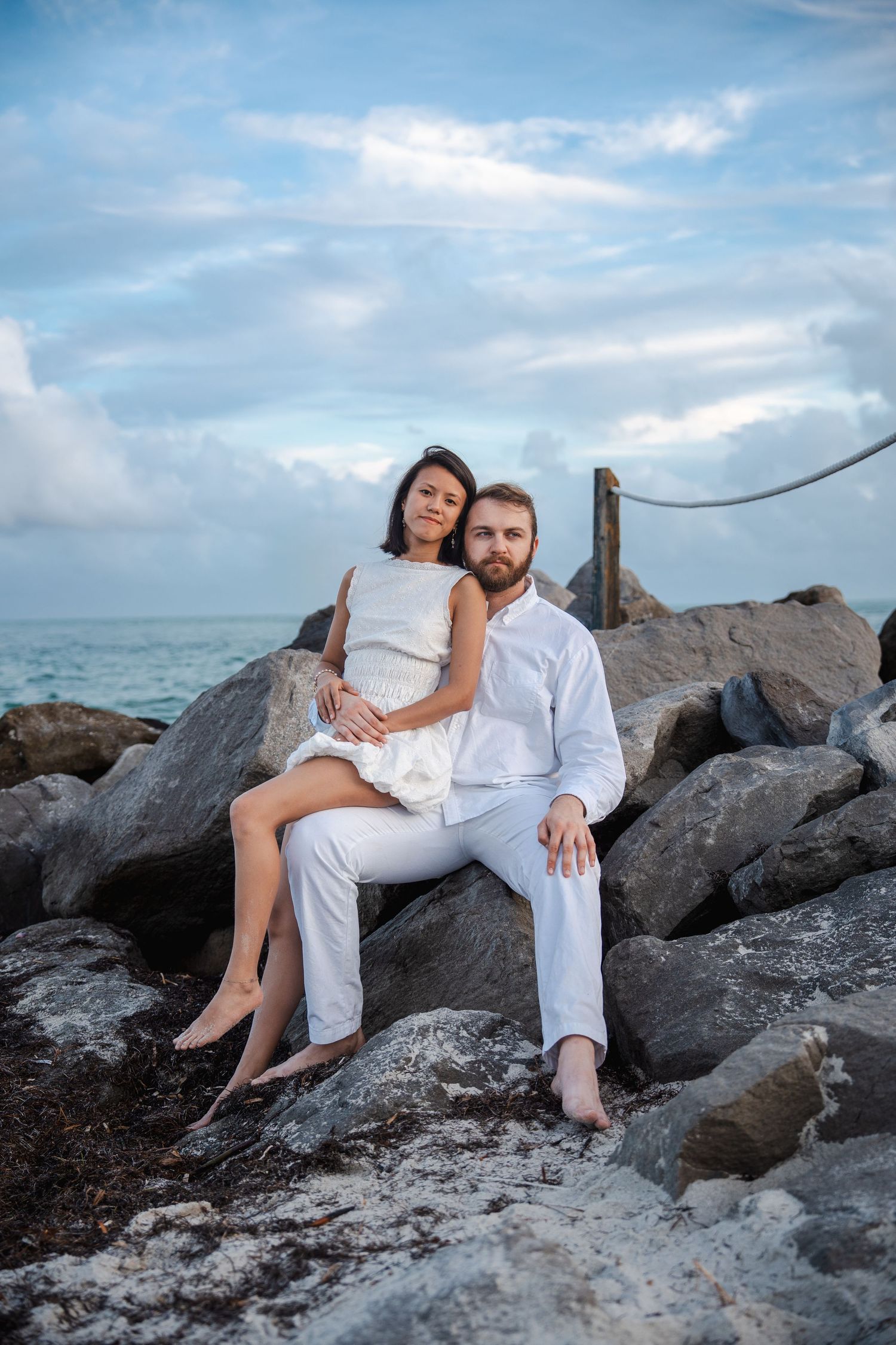 Engagement photo of a couple seated on coastal rocks with ocean views during a romantic South Florida couples session.