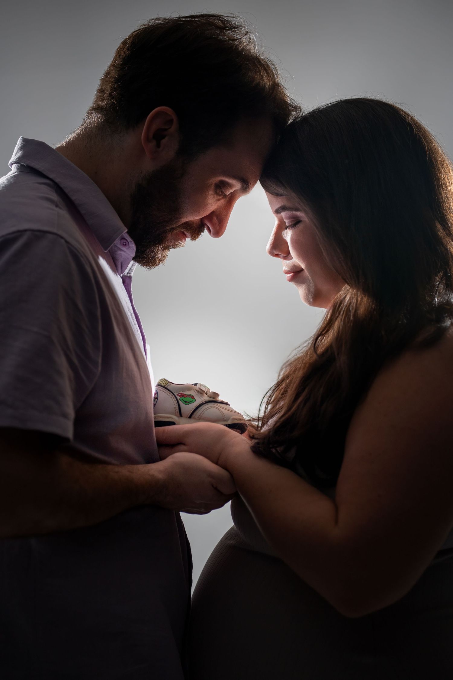 Studio maternity photo of couple touching baby bump under soft light in Miami