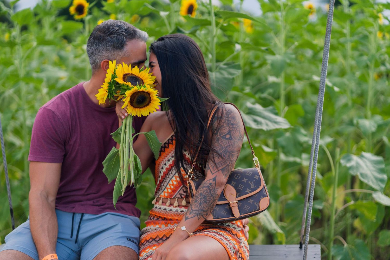 Playful couple’s portrait at Berry Farms in Miami, hiding a kiss behind a vibrant bouquet of sunflowers.