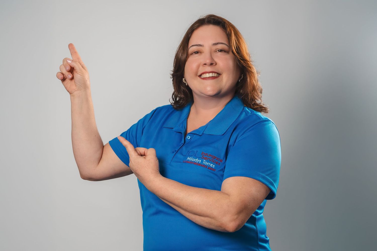 Female team member in matching blue company polo pointing upward in a fun portrait.