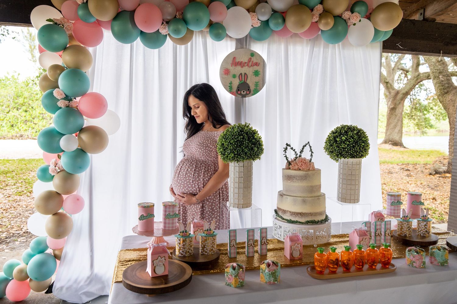 Expecting mother standing behind a styled dessert table at a South Florida baby shower with balloon decor.