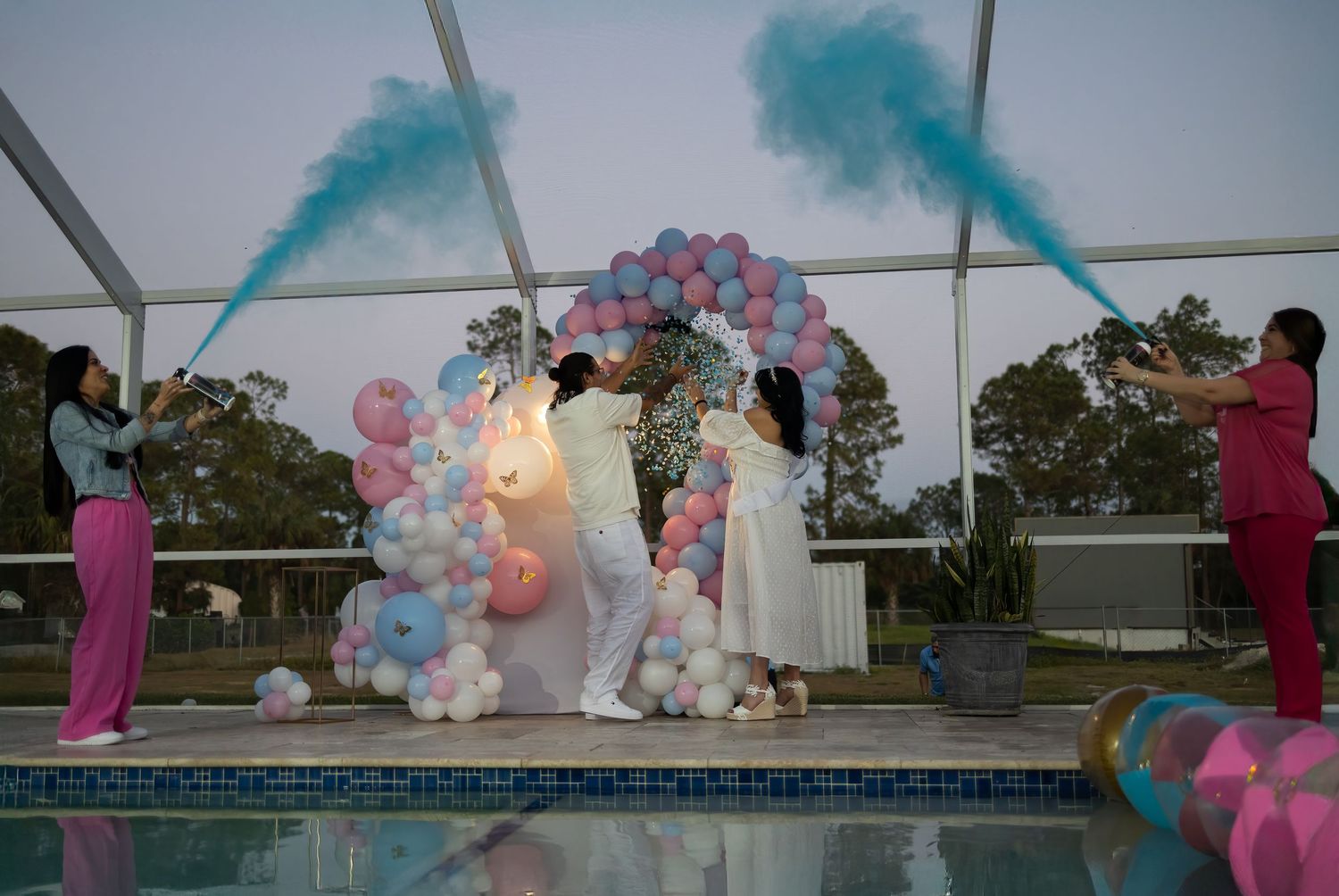 Wide shot of a gender reveal celebration with blue smoke and balloon decor at an outdoor South Florida event.