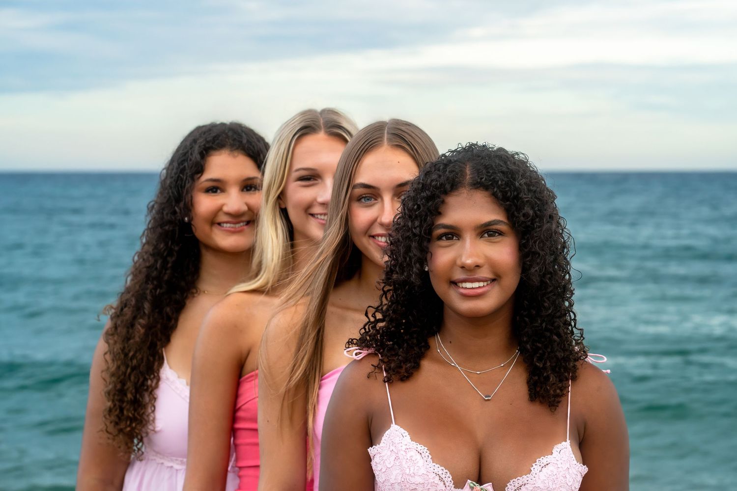 Beach portrait of a cheer squad standing in a line by the ocean during a South Florida team photo session.