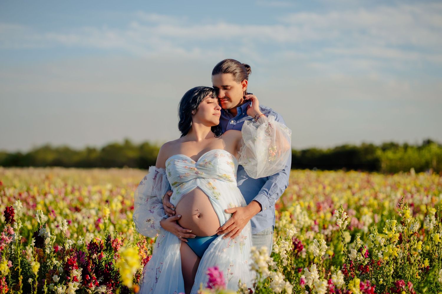 Expecting couple embracing in flower field during maternity portrait session in South Florida