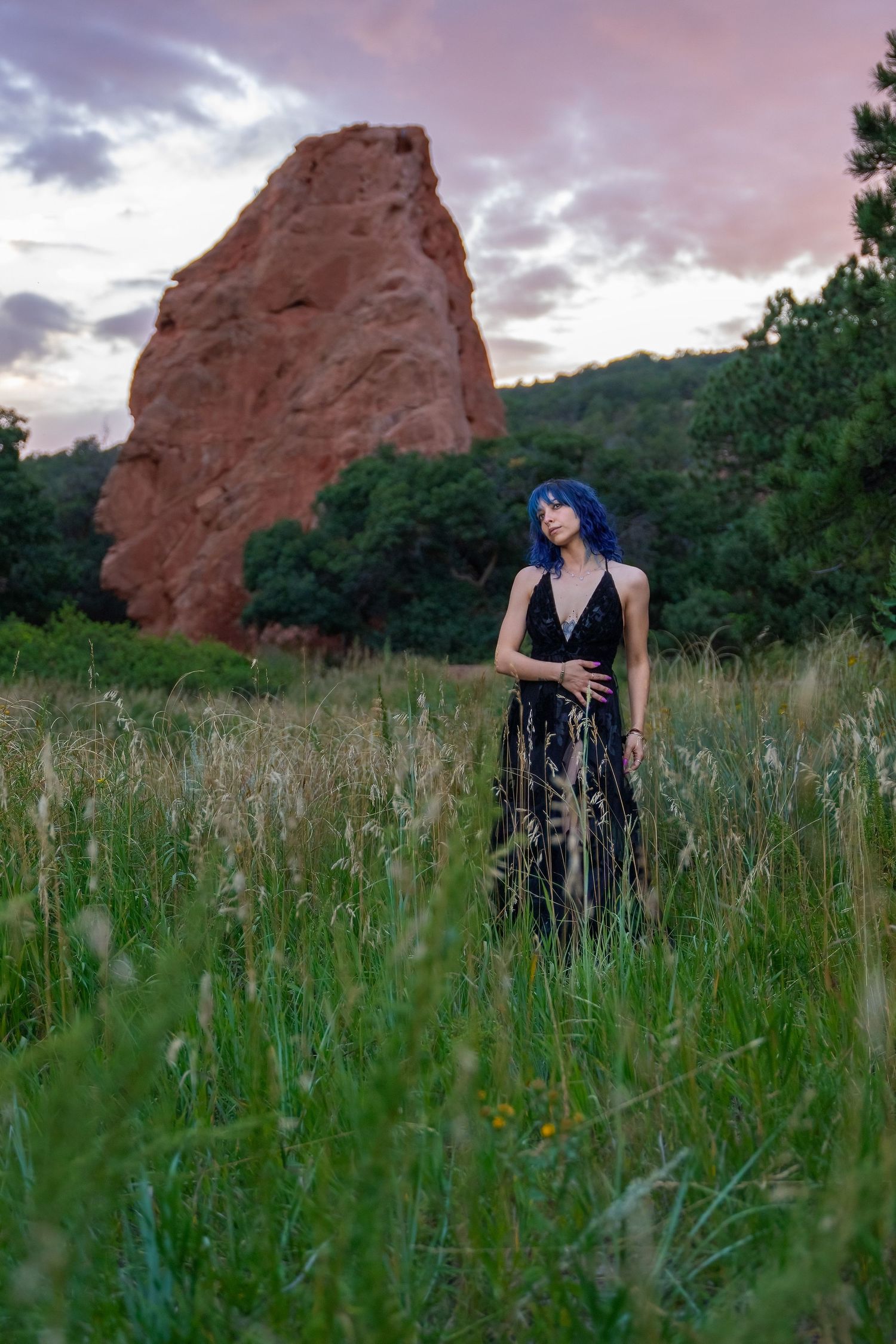 Enchanting scene of a woman in a gothic black dress standing in a lush meadow at Garden of the Gods, framed by towering red rock cliffs.