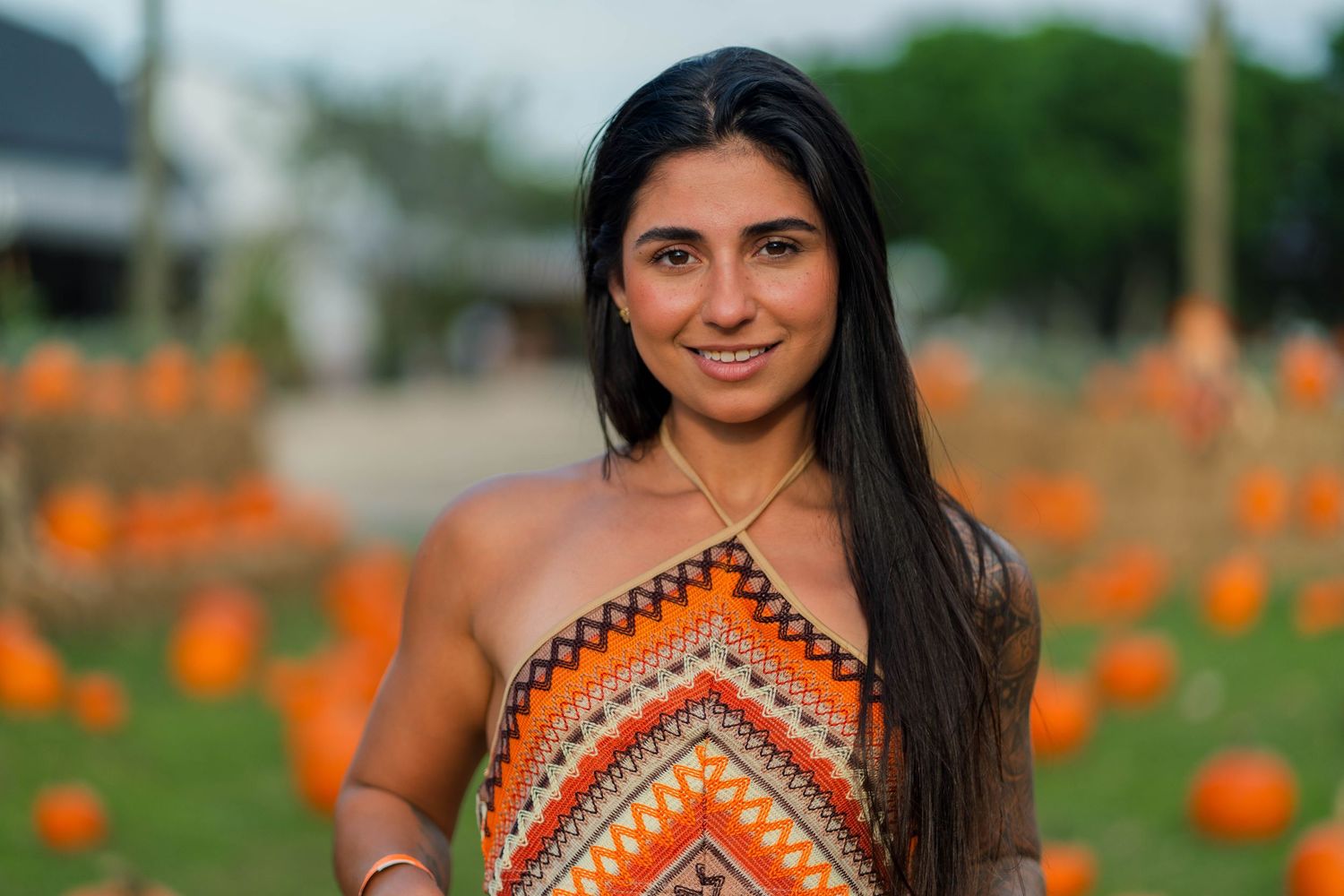 Autumn portrait at Berry Farms, Miami, FL – woman in a patterned dress smiles among pumpkins, capturing fall vibes.
