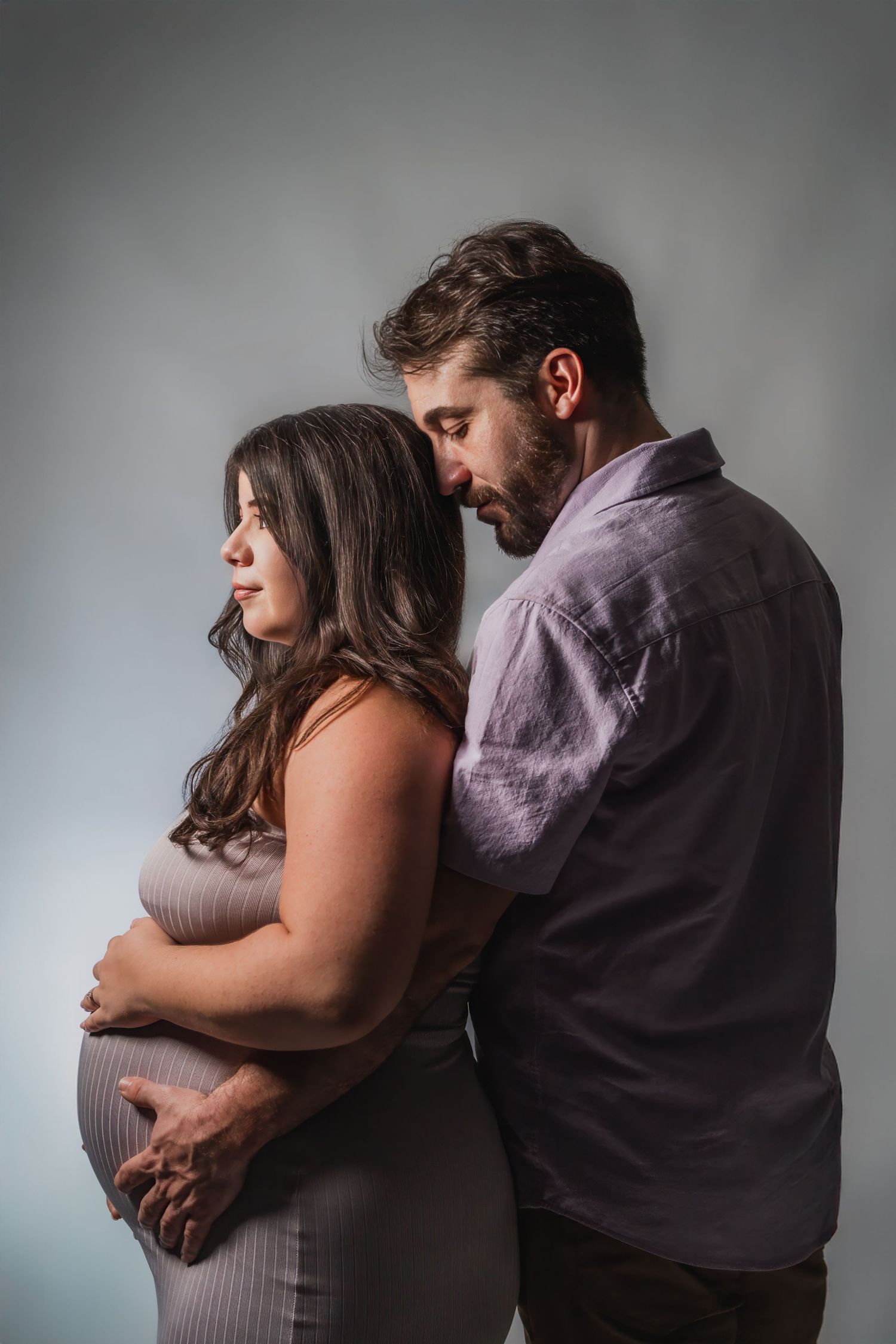 Studio maternity photo of couple touching baby bump under soft light in Miami