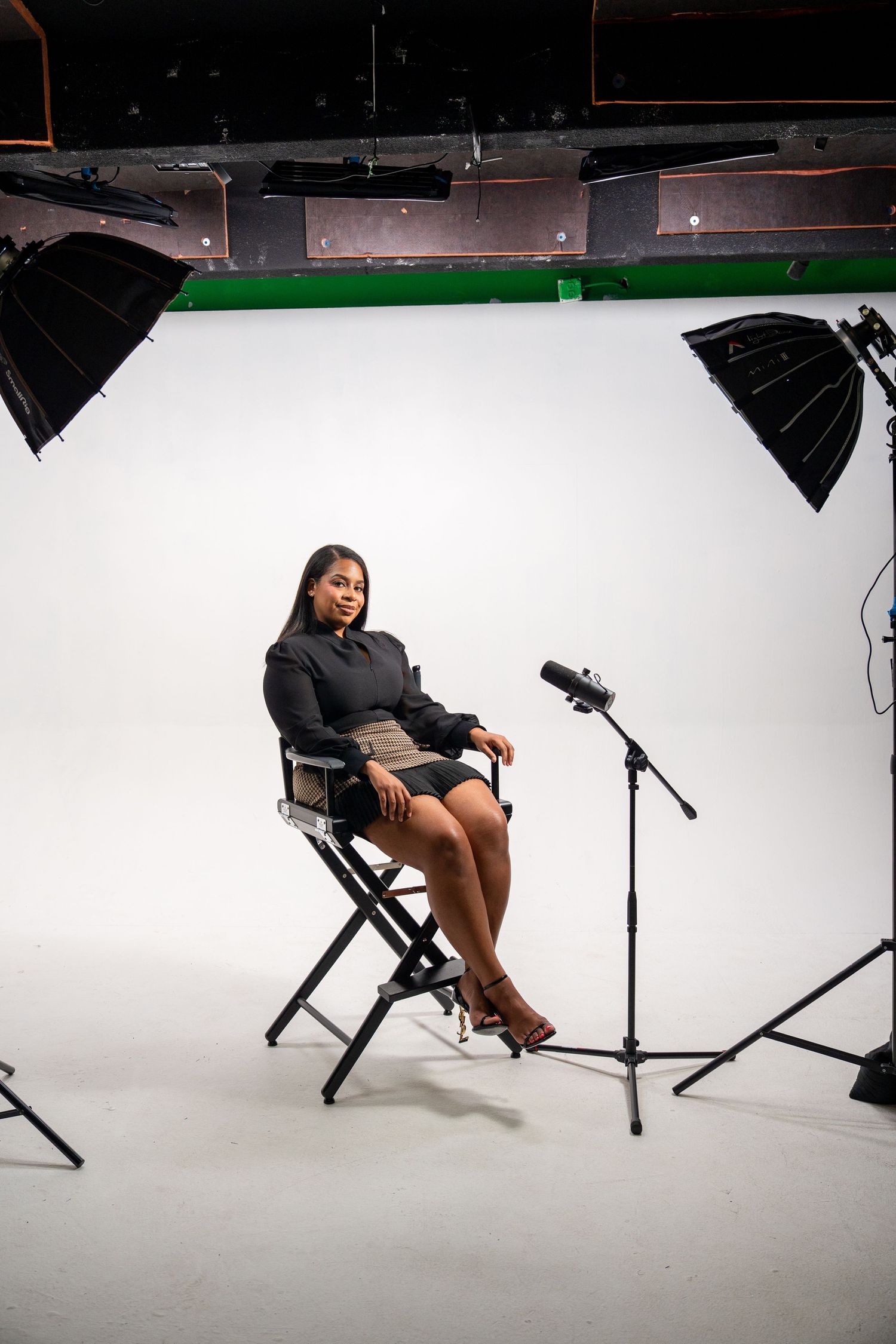Professional branding portrait in a studio setting featuring a woman seated on a chair with lighting equipment visible.
