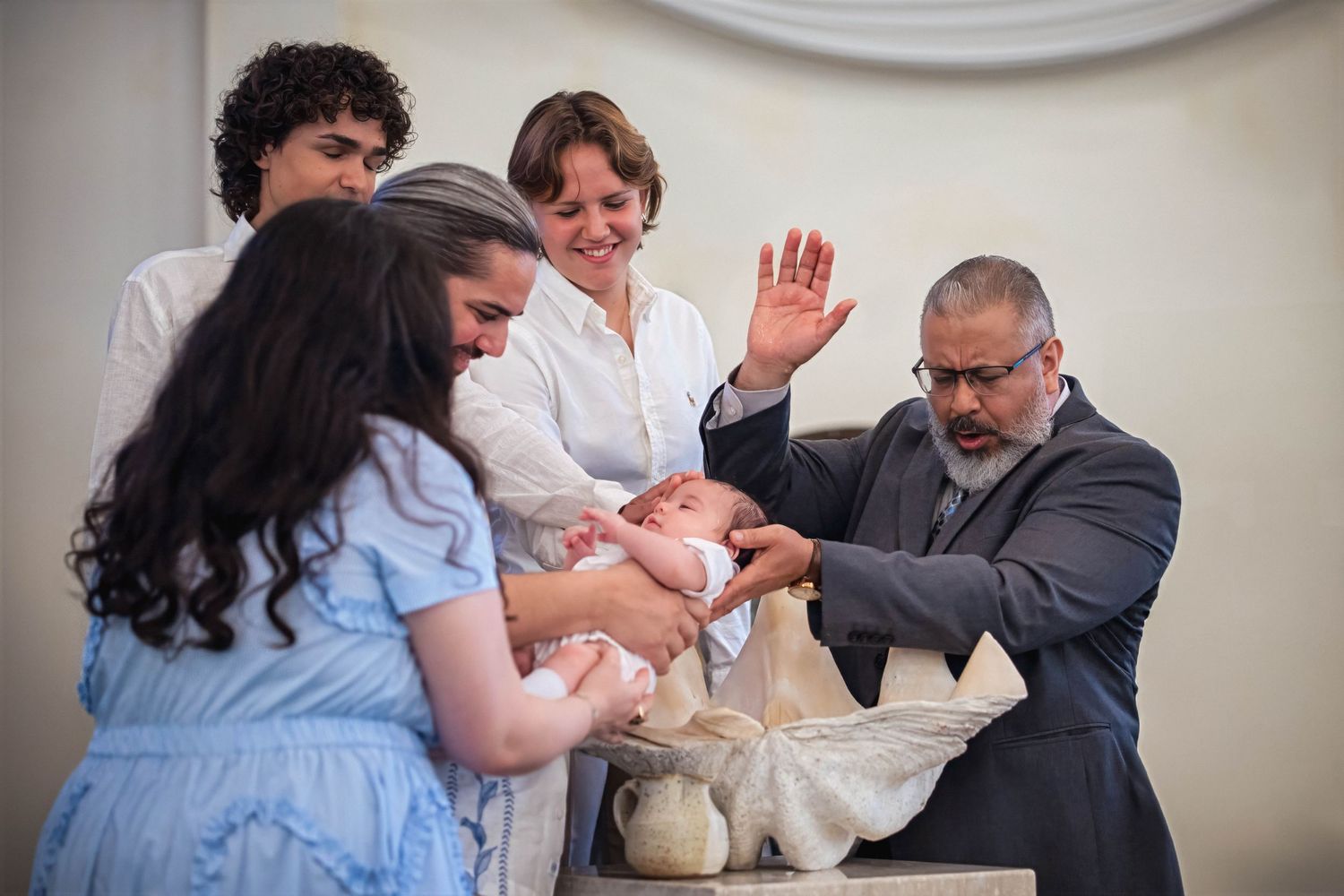 Baptism ceremony moment with family gathered around the baptismal font inside a church.