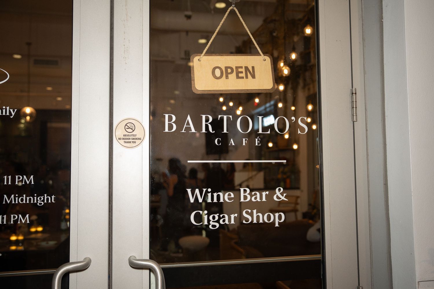 Close-up of the entrance doors to Bartolo’s Wine Bar & Cigar Shop displaying the open sign and venue branding.
