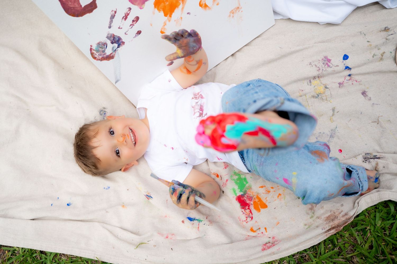 Toddler covered in paint and laying on a canvas tarp during a messy and fun family session.