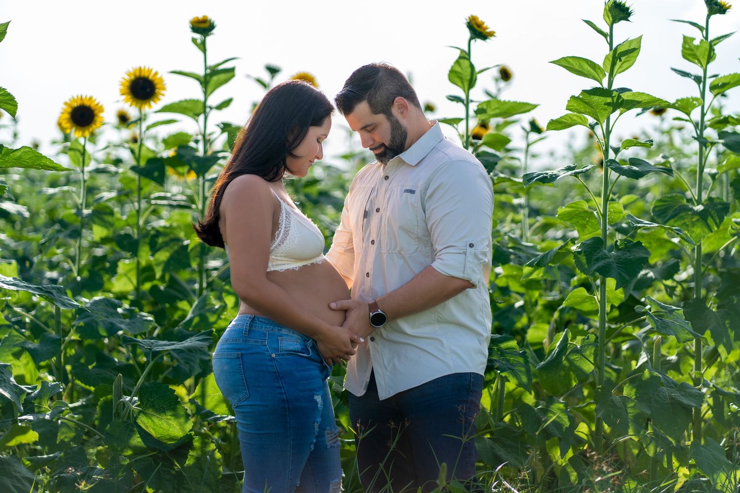 Romantic maternity session in Homestead, capturing an intimate embrace surrounded by tall, golden sunflowers.